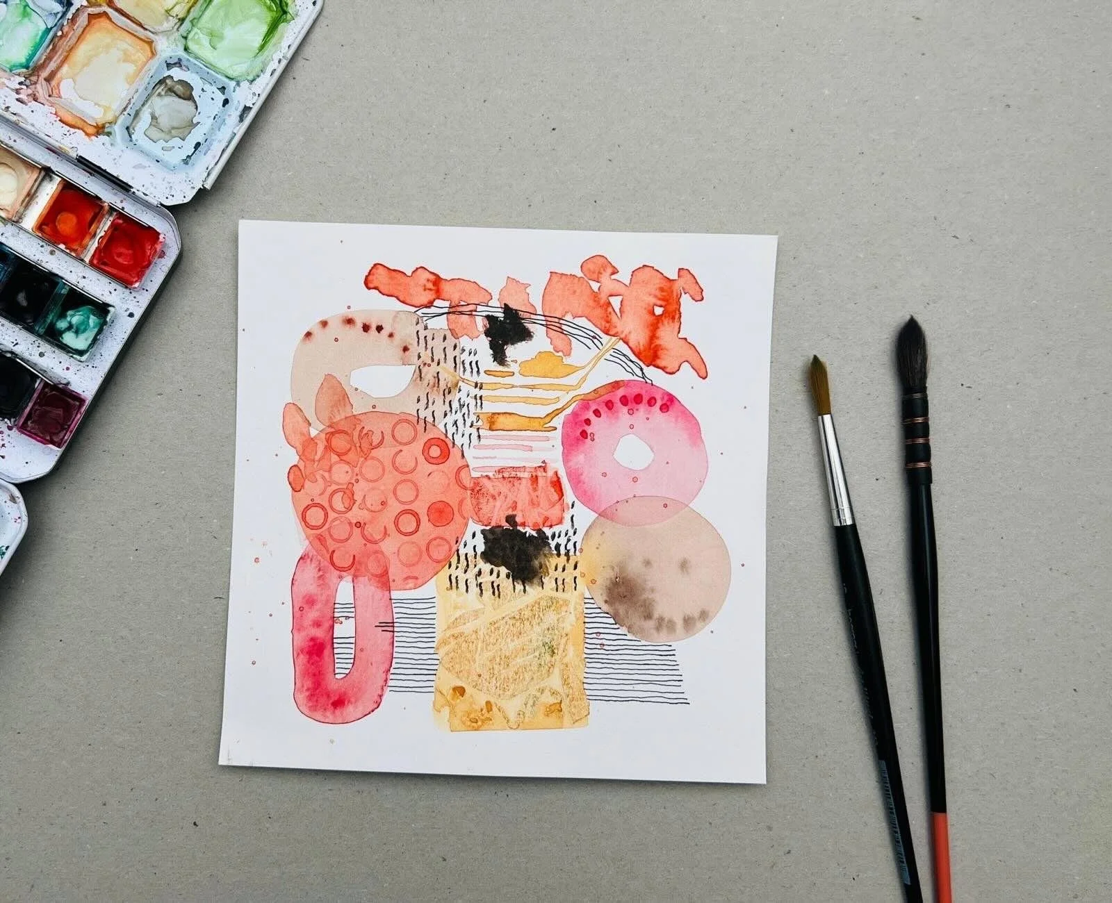 abstrakte Aquarellmotive in rot, rosa,gelb, Striche in schwarz. Aquarellkasten und zwei Pinsel