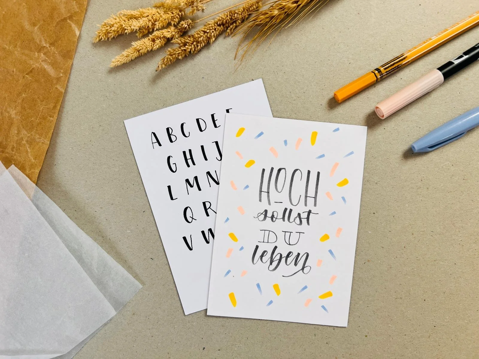 Zwei handschriftliche Karten mit Alphabet auf weißem Papier und Spruch 'Hoch sollst du leben, auf weißem Papier mit gemalten Konfetti.