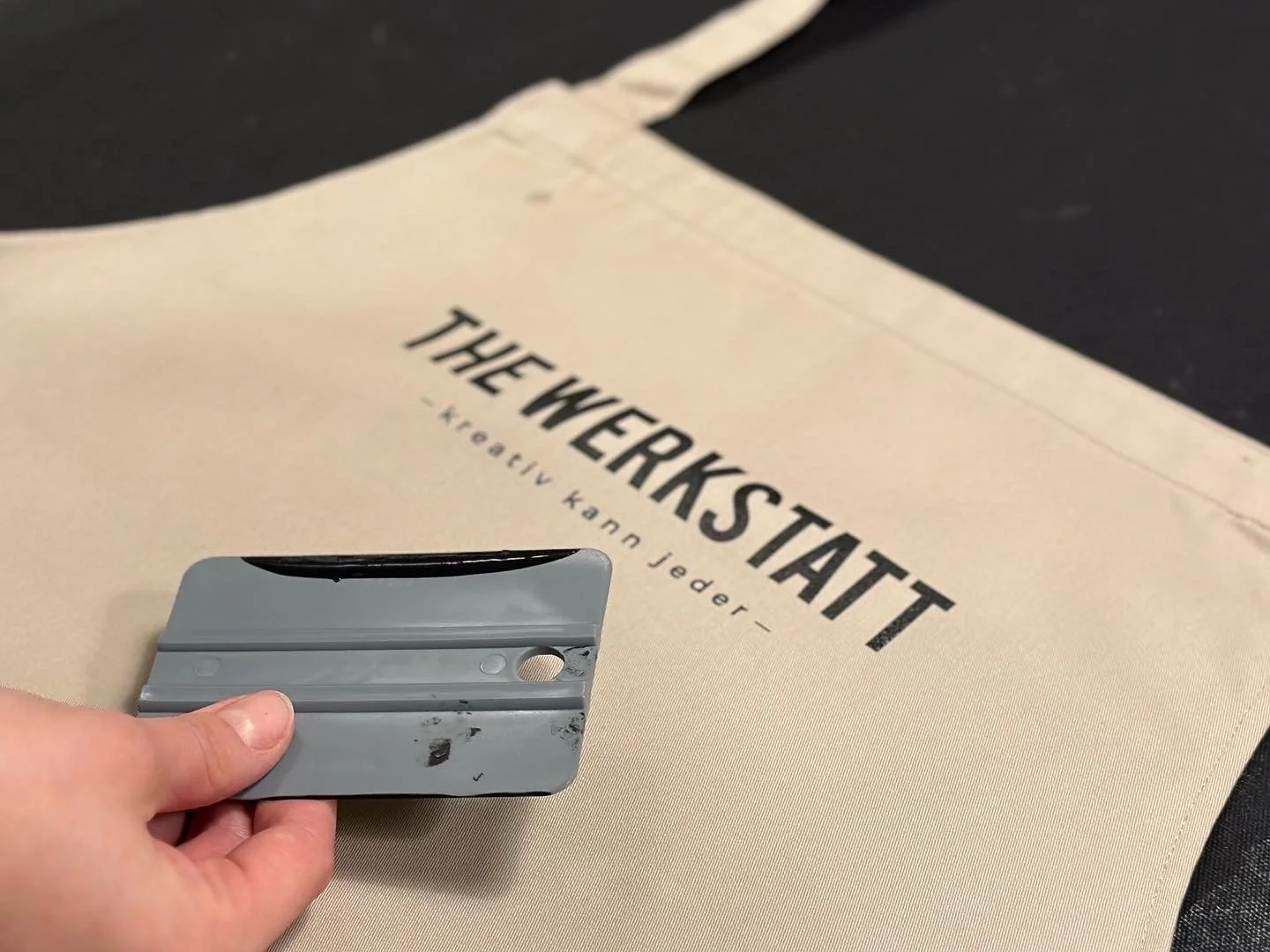 Hand hält Rakel über eine Schürze mit der Schrift 'The Werkstatt'