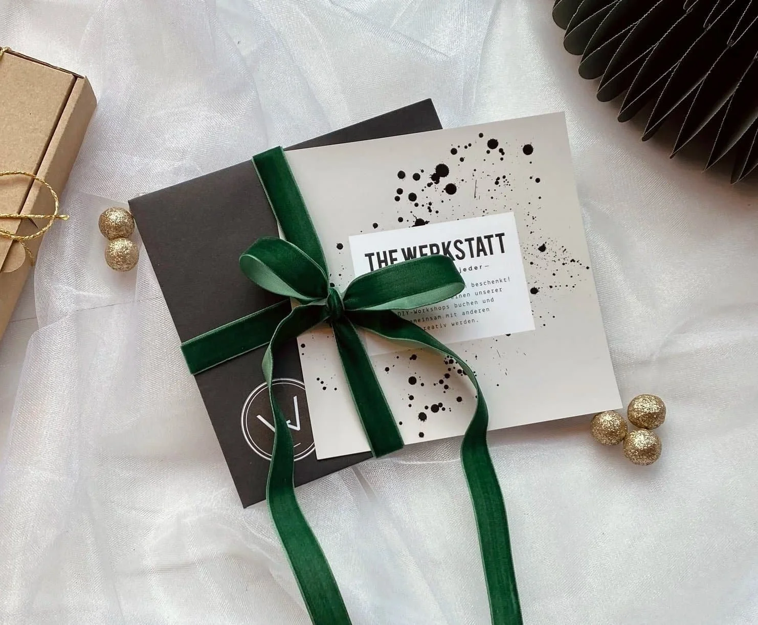 Geschenkgutschein mit grünem Satinband, mit einem Schwarz-Weiß-Design und schwarzem Text, umgeben von goldfarbenen Dekos.