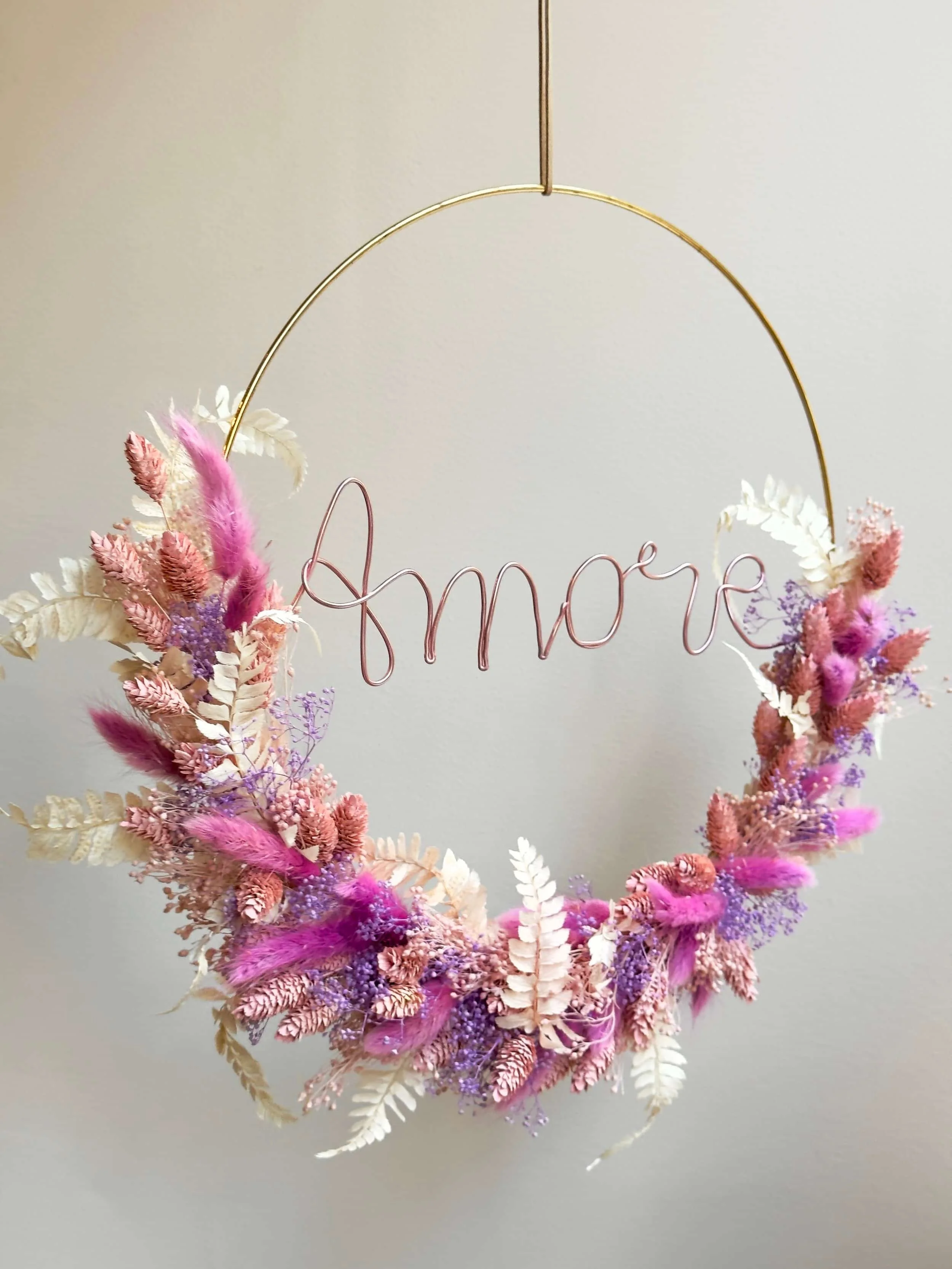 Trockenblumenkranz in weiß, lila und rosa auf einem Drahtkreis mit Drahtlettering des Wortes "Amore"