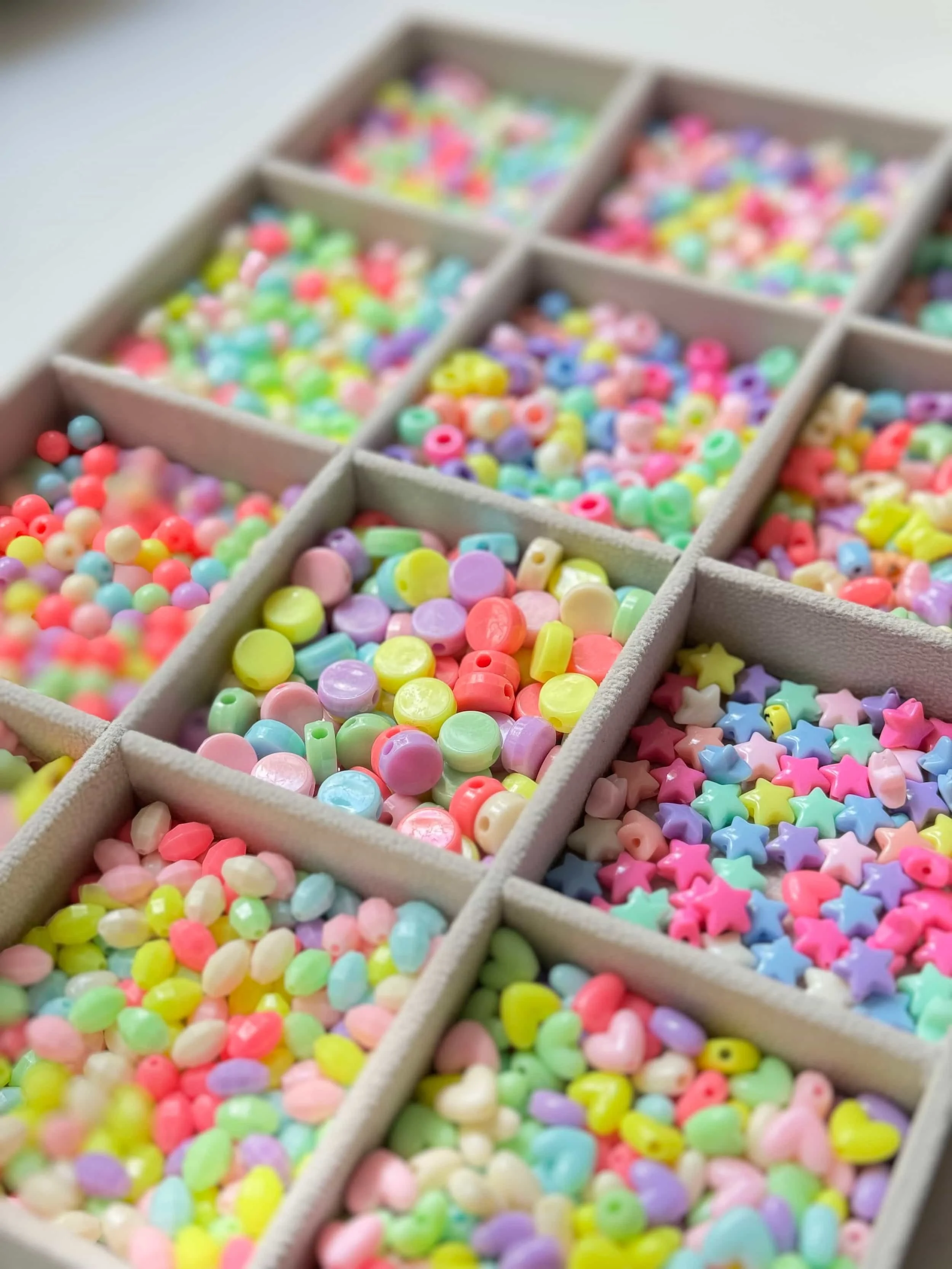 Bunte Kunststoffperlen in ruhigeren Tönen von lila, gelb, grün, rot und veschiedenen Formen wie Stern, Oval, kreis, Herz