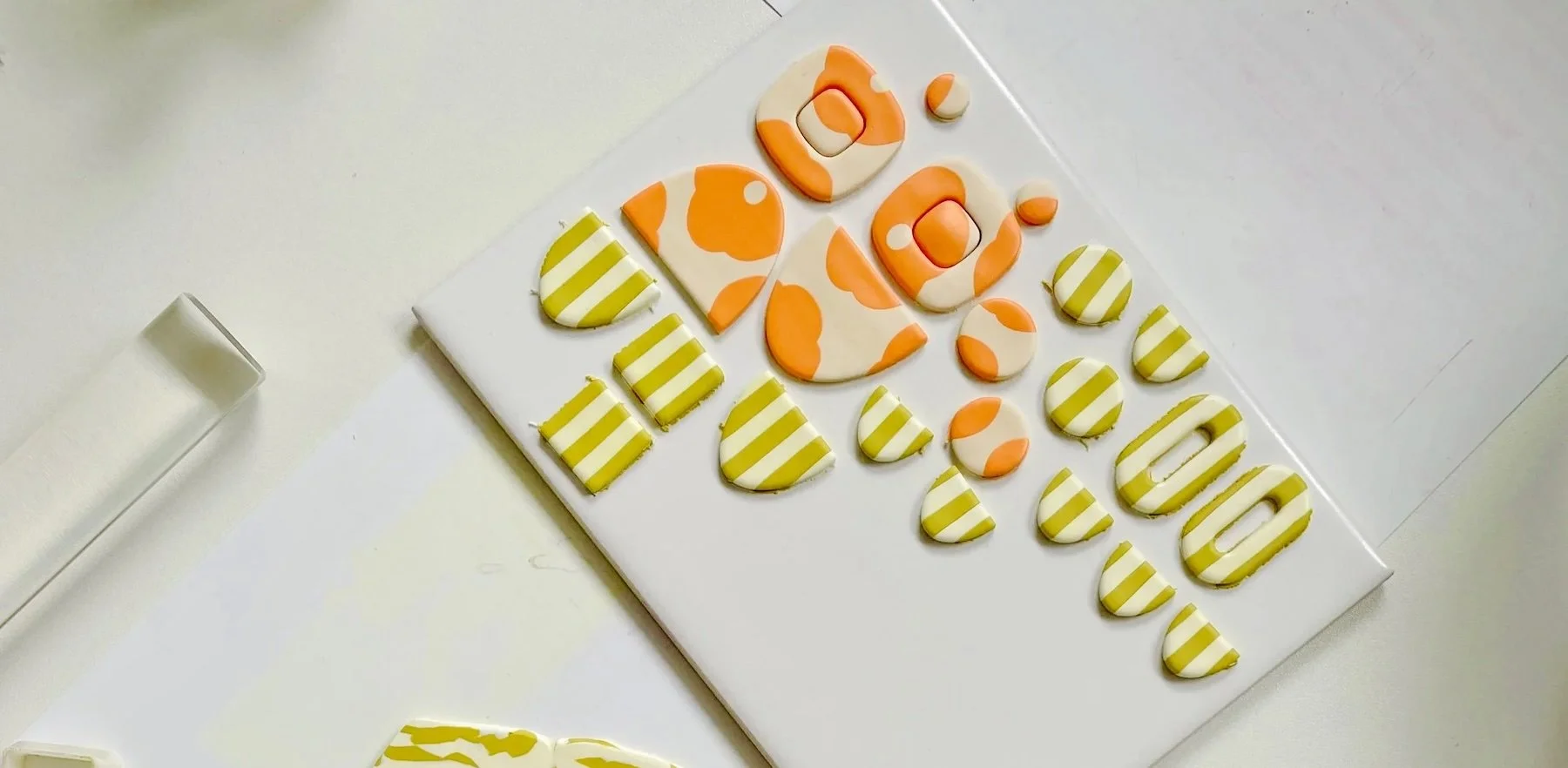 bunte Abschnitte aus Polymer Clay Masse liegen auf dem Tisch neben Acrylroller und anderen Tools