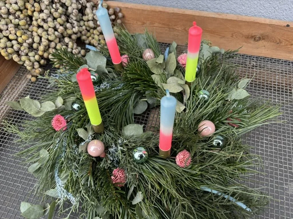 Adventskranz aus Tannenzweigen mit kleinen Weihnachtskugeln und vier bunten Kerzen