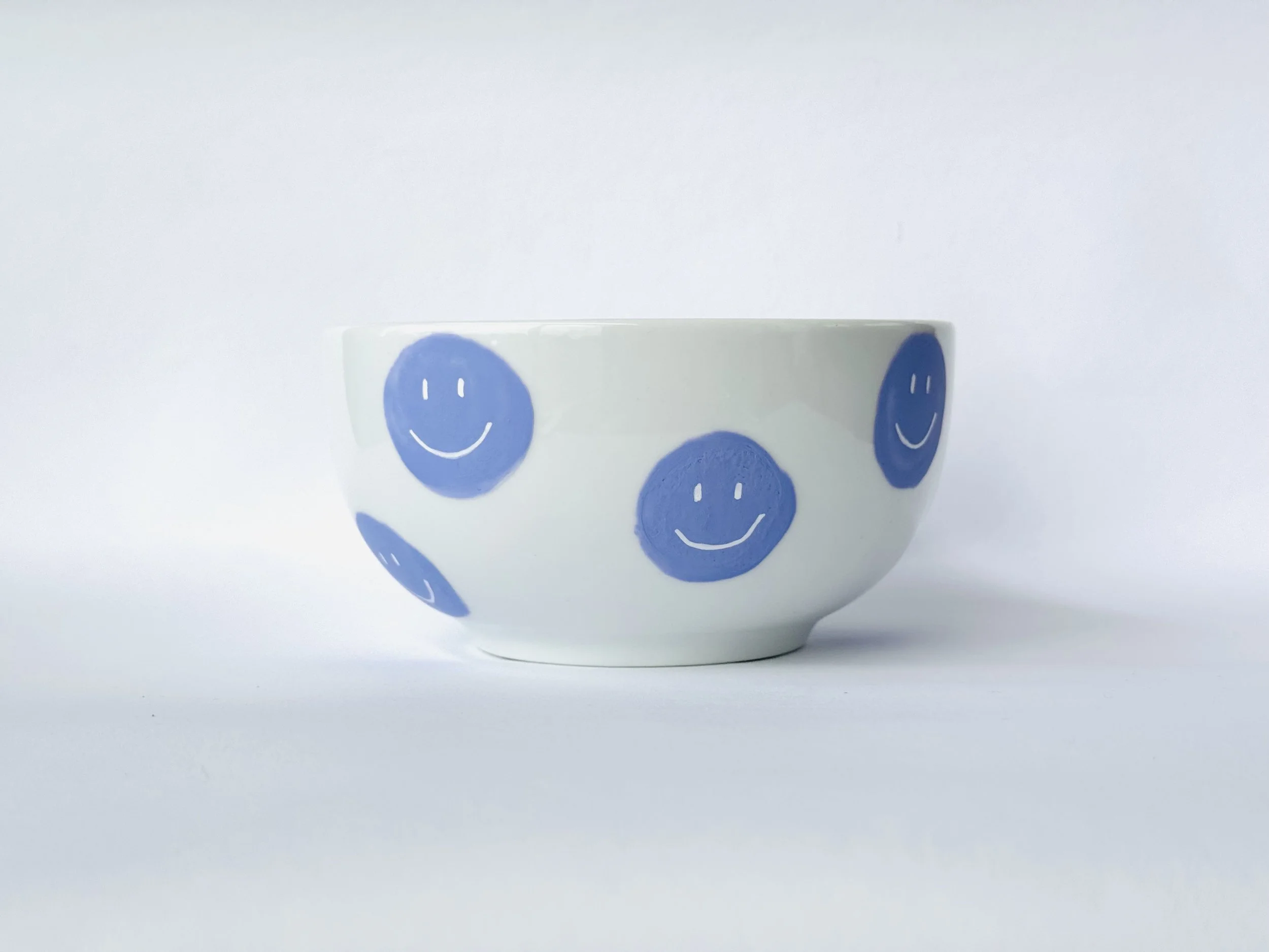 Weiße Porzellanschale mit blauen Smiley-Gesichtern gegen weißen Hintergrund.