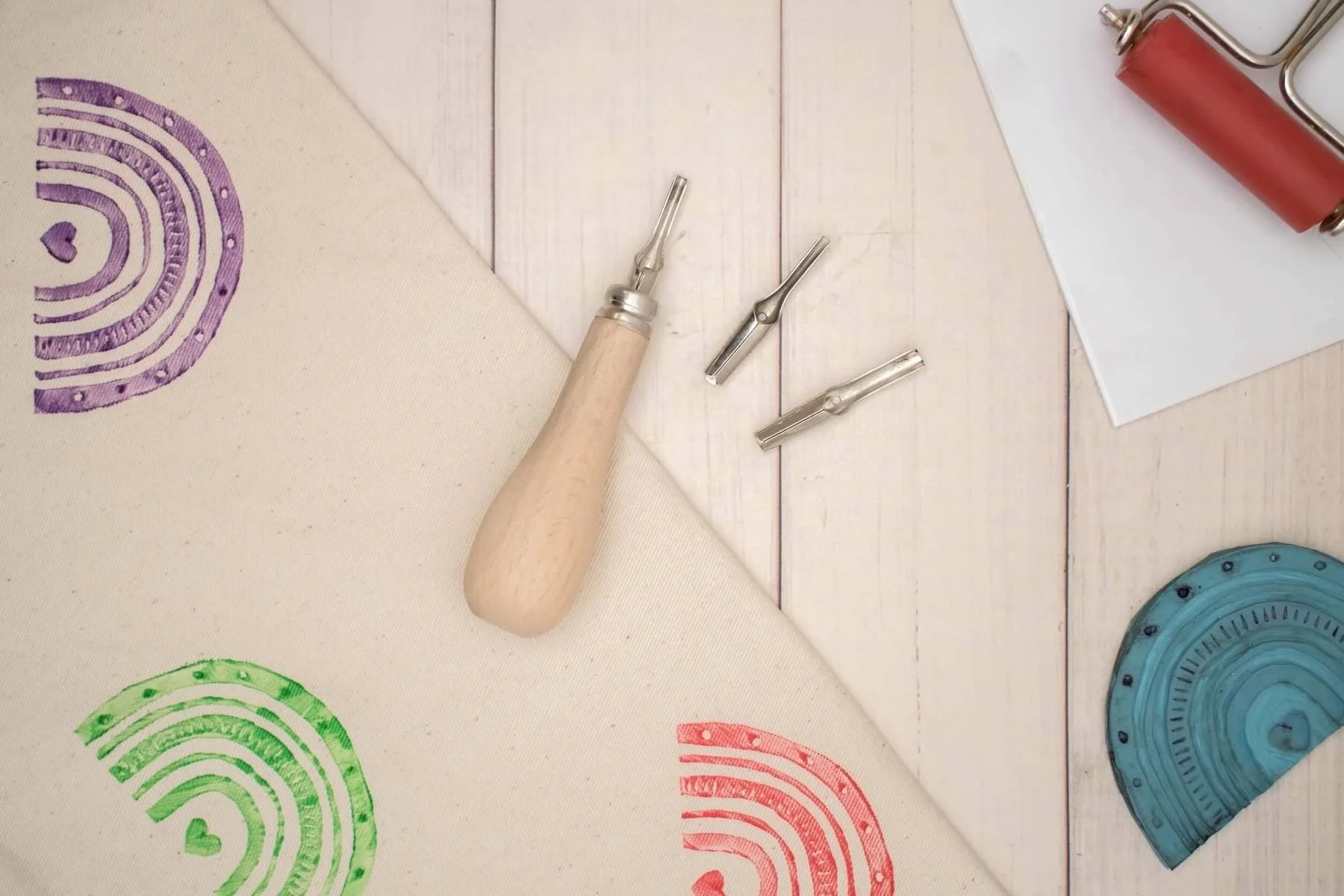 Stempel, Stempelkissen, Stempelfolie, Holzstiel, Stempelmesser, Papier, Holzboden, Stoff mit Fingerabdruckmotiven in Lila, Grün, Rot, Blau.