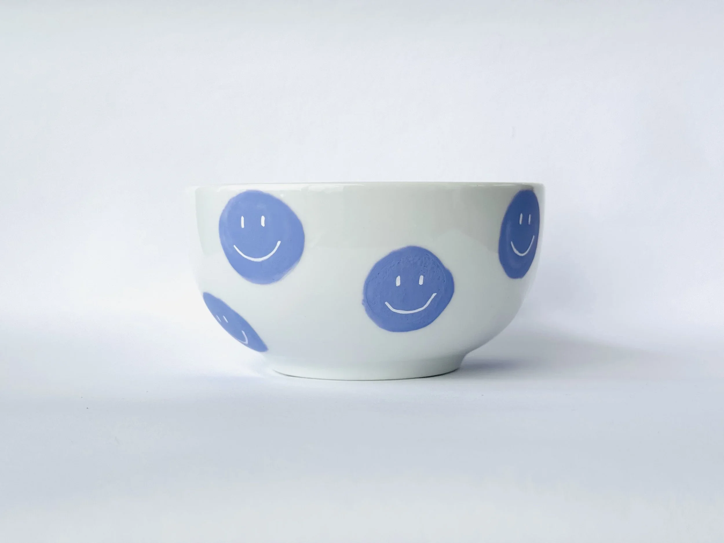 Weiße Porzellanschale mit blauen Smiley-Gesichtern gegen weißen Hintergrund.
