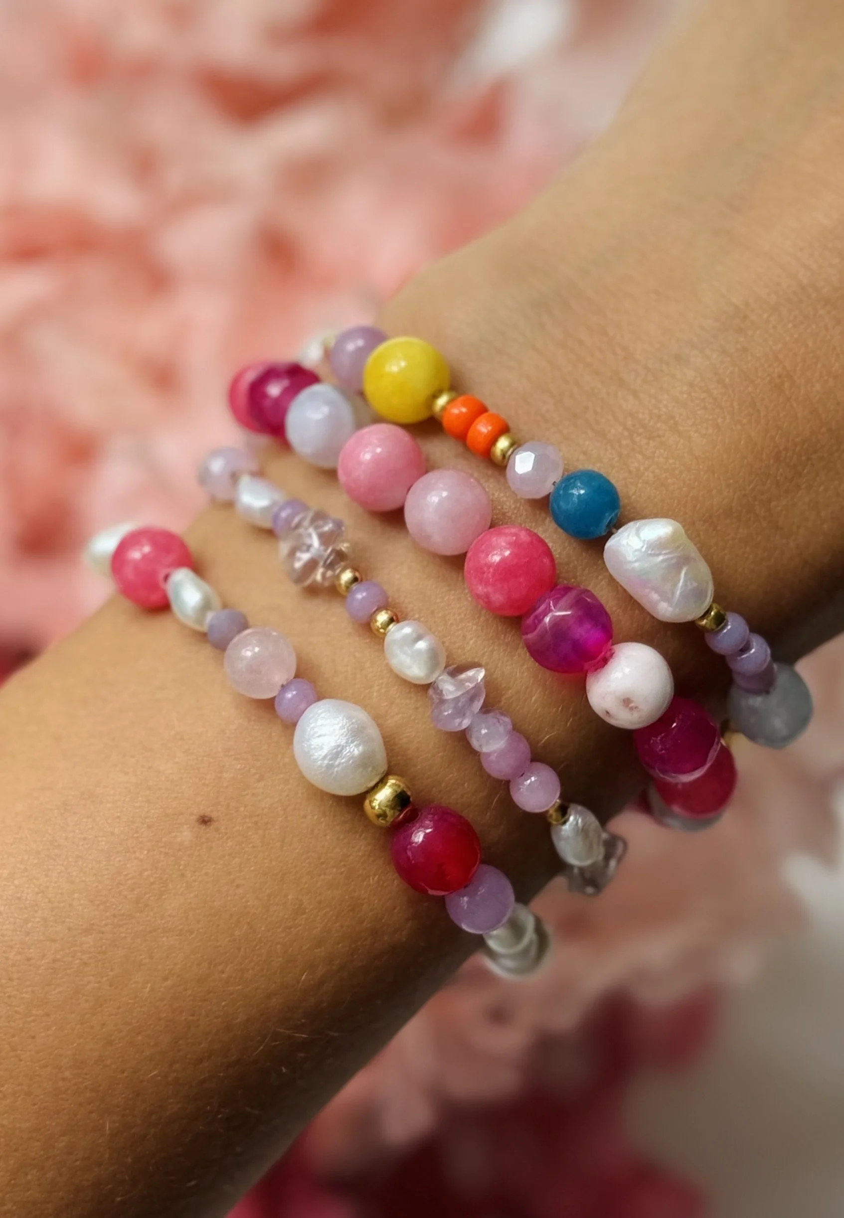 Bunte Perlenarmbänder um das Handgelenk einer Person, mit pinken, weißen, gelben, blauen und roten Perlen.