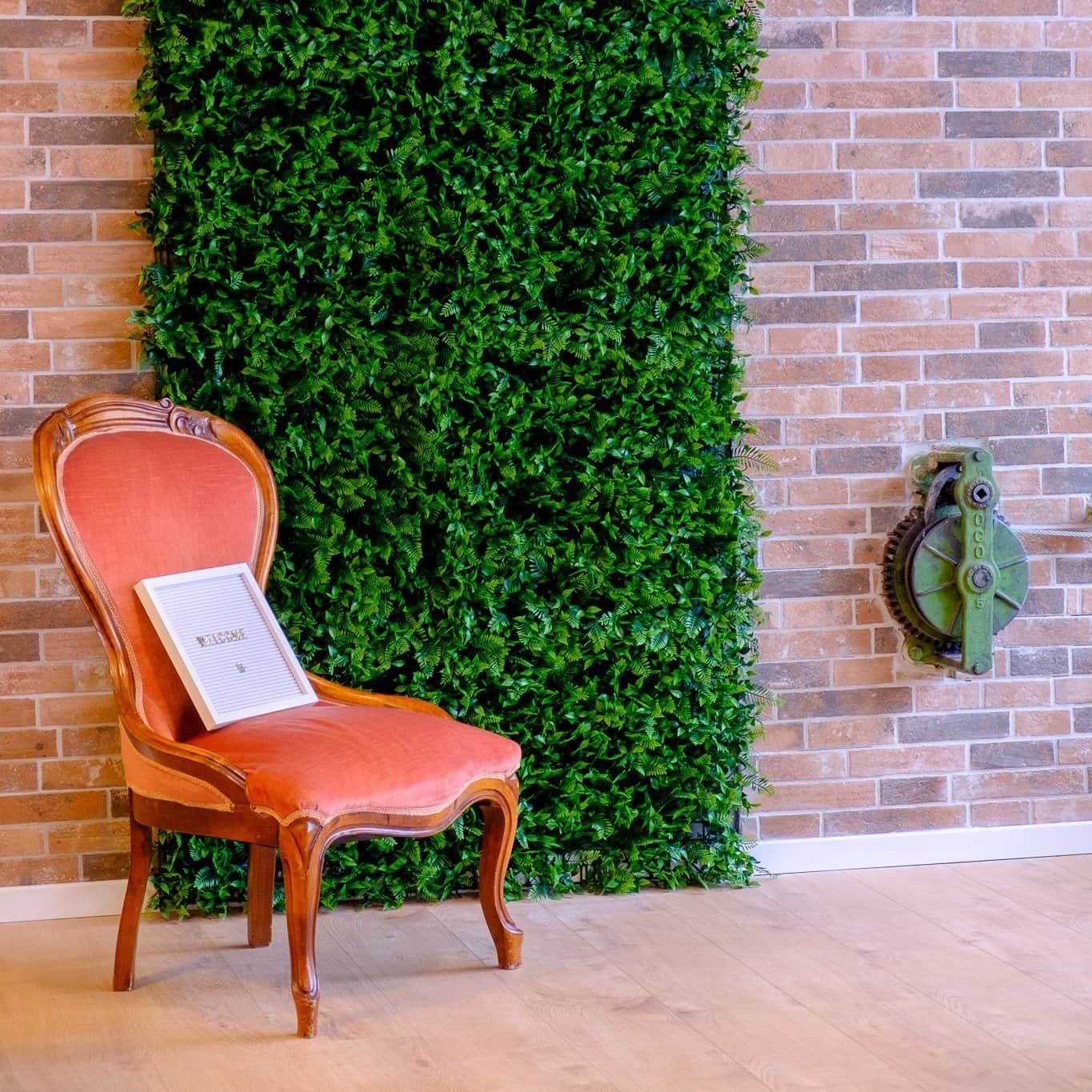 Ein antiker Stuhl mit rotem Bezug, eine grüne Wanddekoration aus lebendigem Blattwerk, eine Wand aus Ziegelsteinen und ein mechanisches Gerät an der Wand.