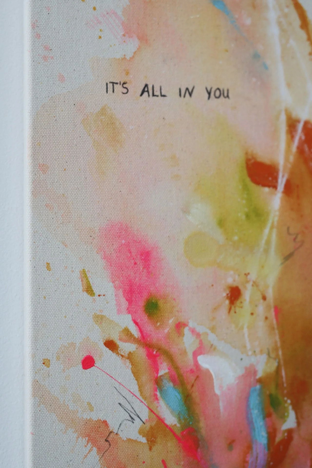 Ein abstraktes Kunstwerk mit bunten Farbklecksen und Pinselstrichen, das den Spruch 'IT'S ALL IN YOU' enthält.