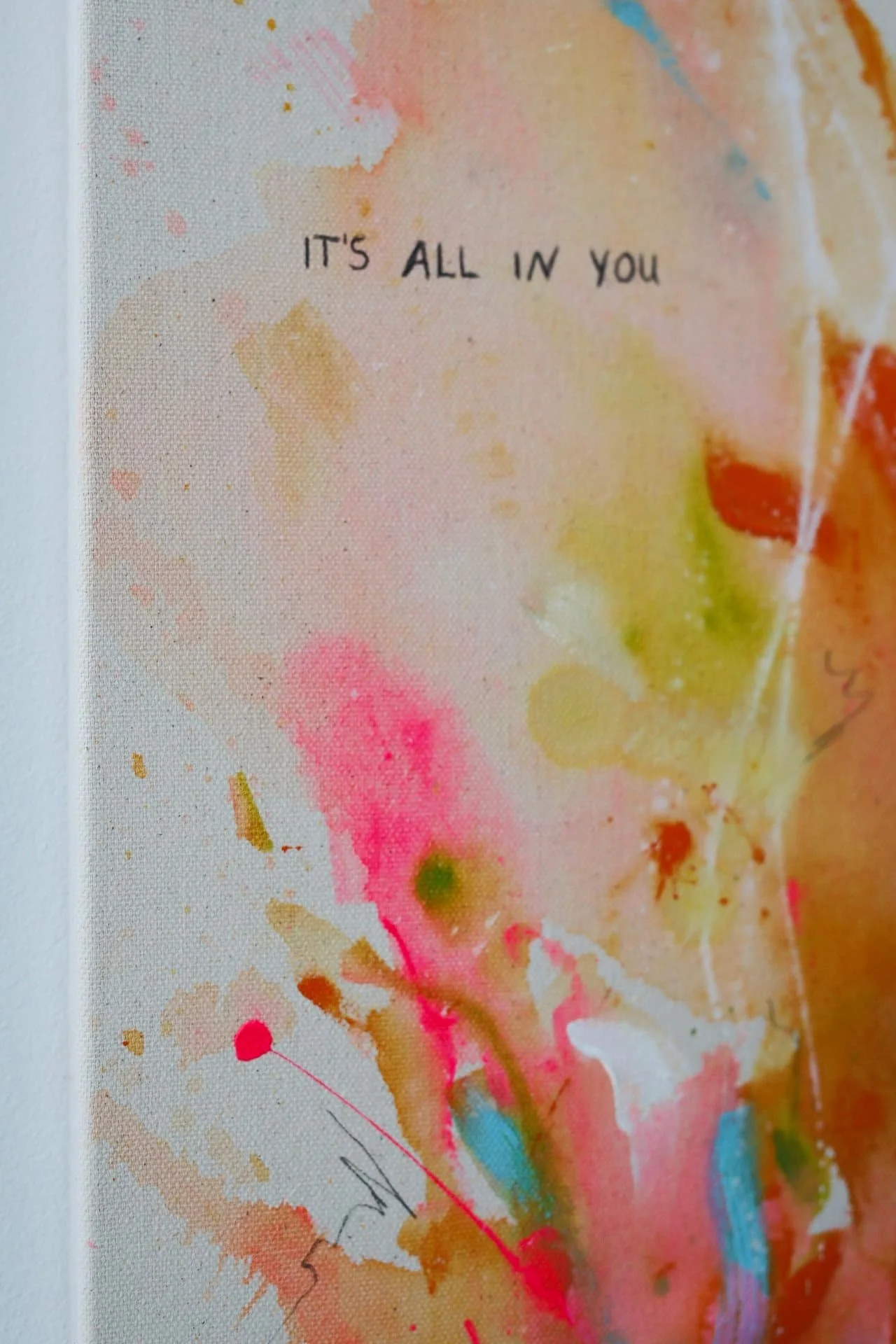 Ein abstraktes Kunstwerk mit bunten Farbklecksen und Pinselstrichen, das den Spruch 'IT'S ALL IN YOU' enthält.