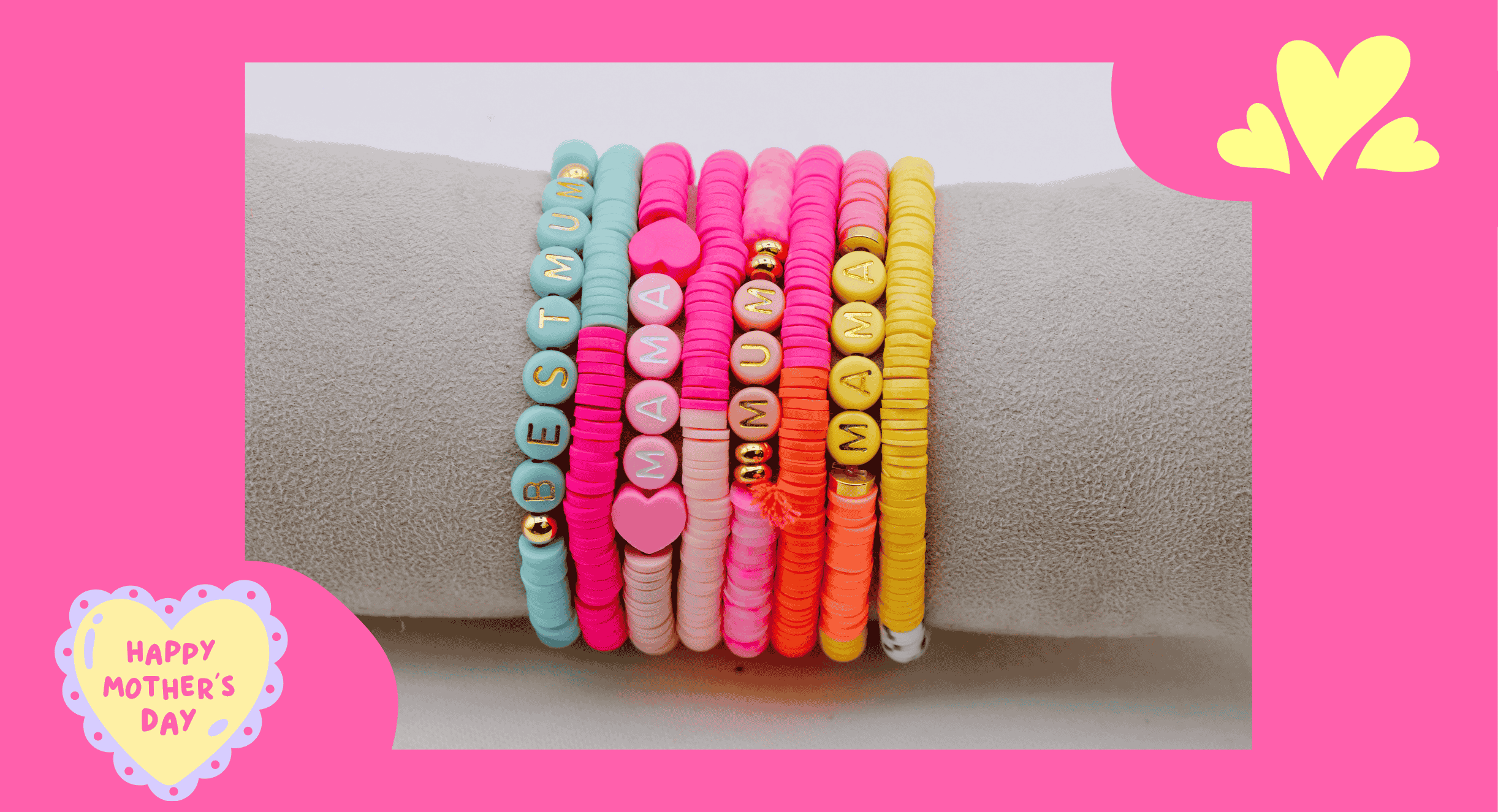 Viele bunte Armbänder auf einem aus Samt bezogenen Träger, heller Hintergrund, Rahmen in rosa. Text 'Happy Mother's Day'