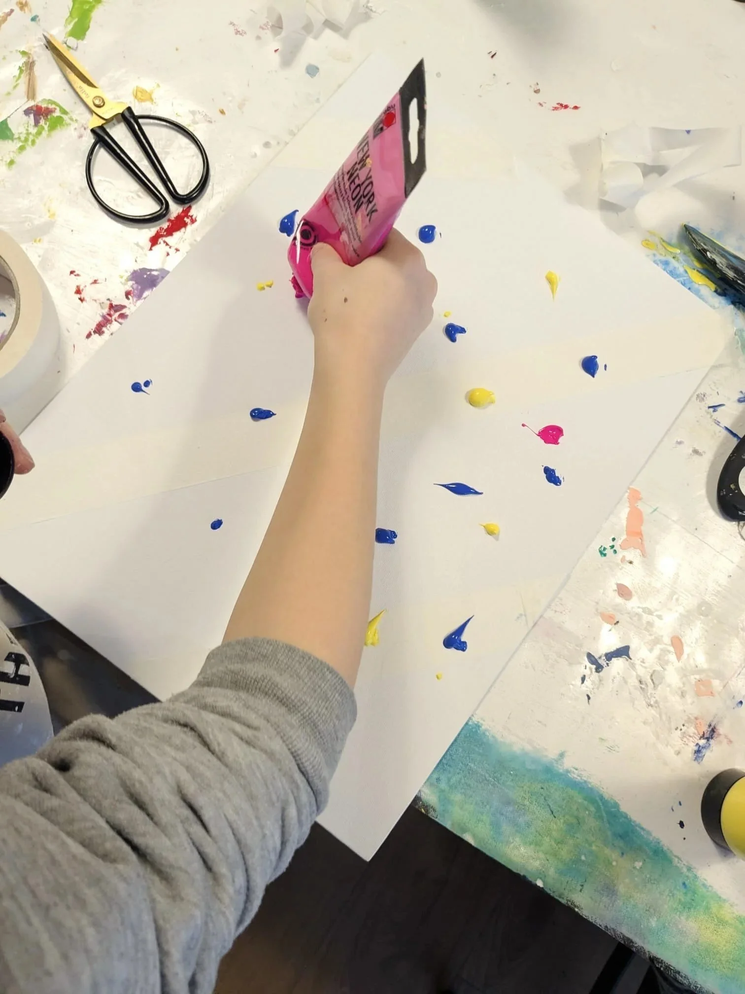Hand, die Kleckse mit Acrylfarben auf einer Leinwand setzt.