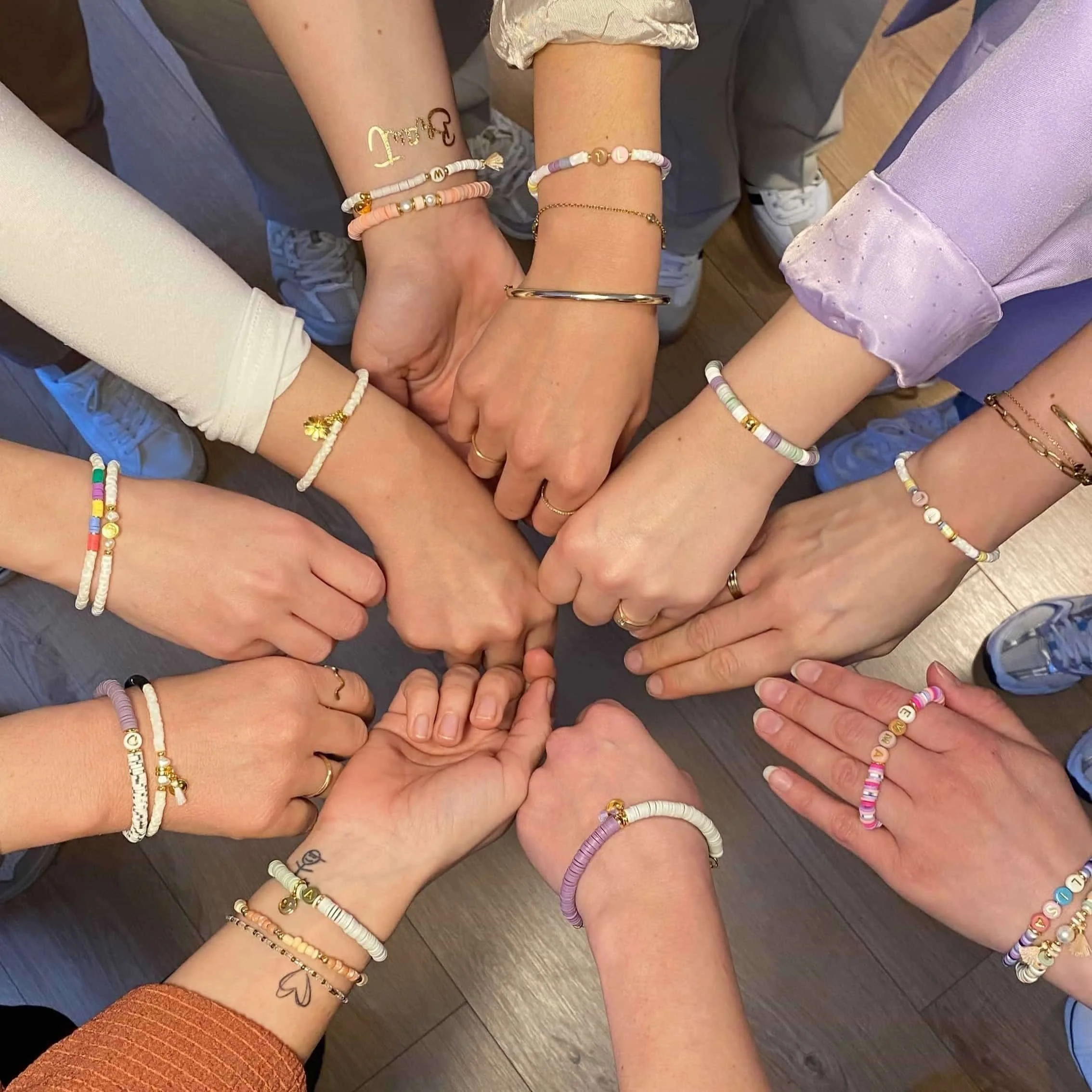 Zehn Arme, die ihre Hände in die Mitte strecken und selbstgemachte Katsuki-Armbänder tragen