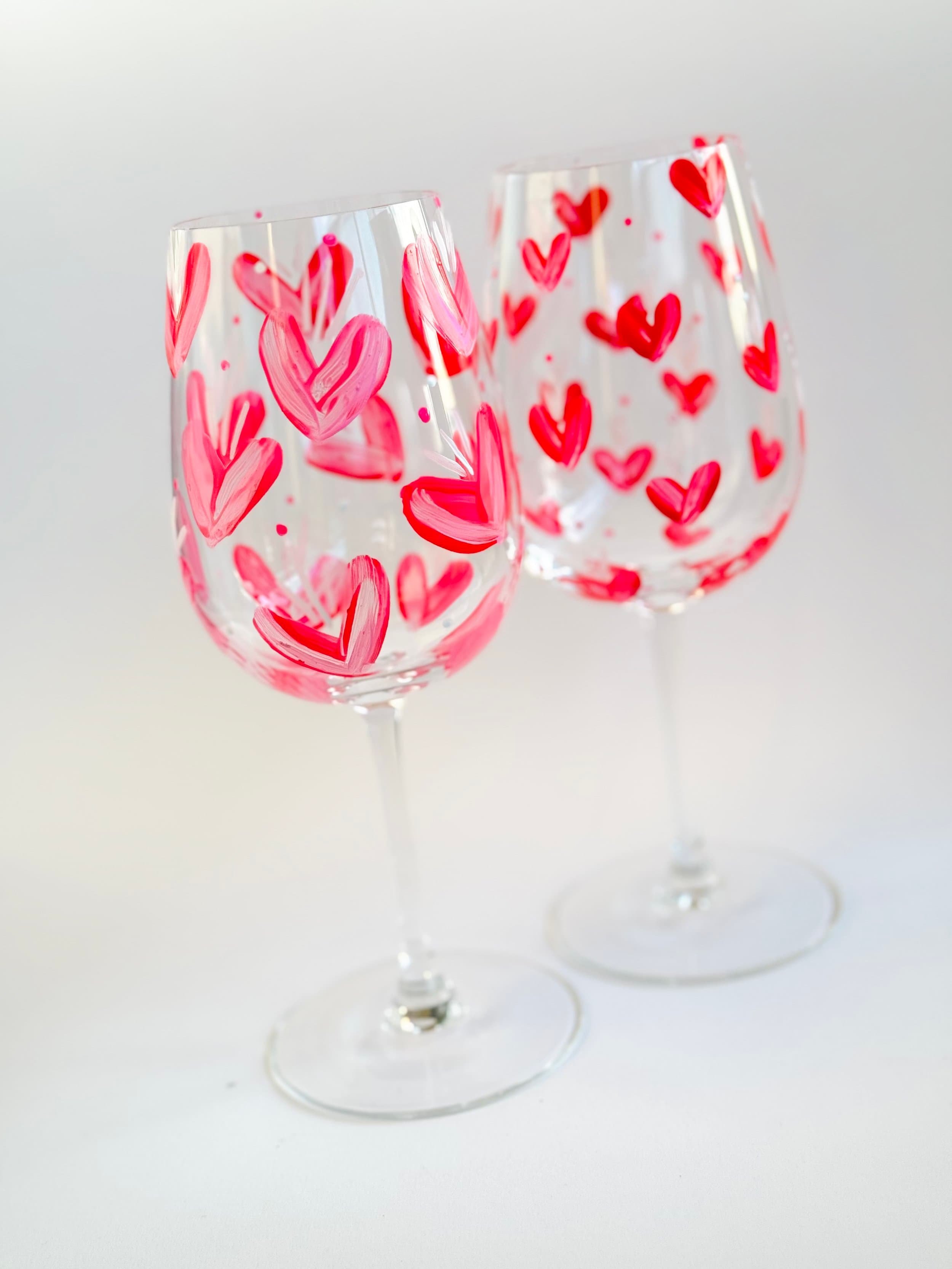 Zwei Weingläser mit roter und pinker Herzdeko, gegen weißen Hintergrund.