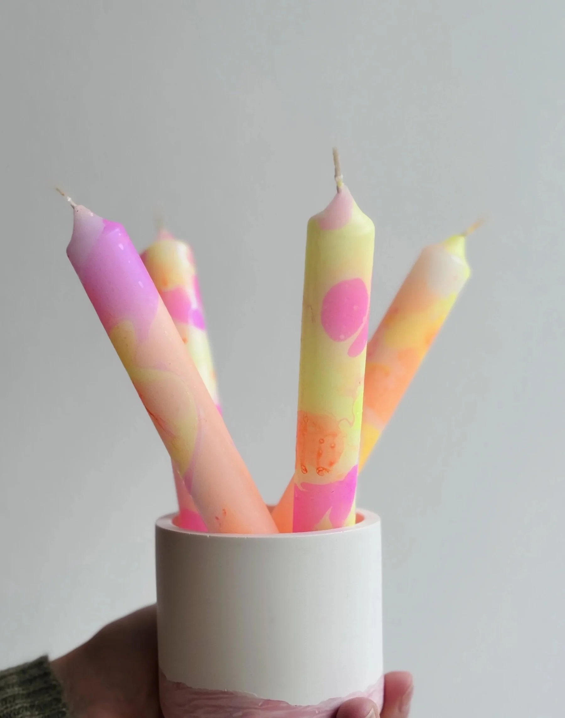 Vier bunte Kerzen in neon pink, gelb, orange stehend in einem Becher