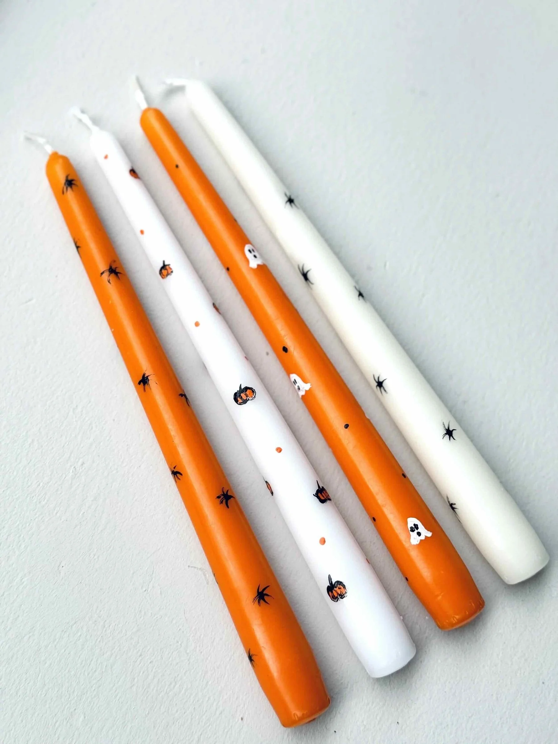 Vier Spitzkerzen in weiß, orange bemalt mit verschiedenen Halloween Motiven wie Kürbis; Gespenst, Netz