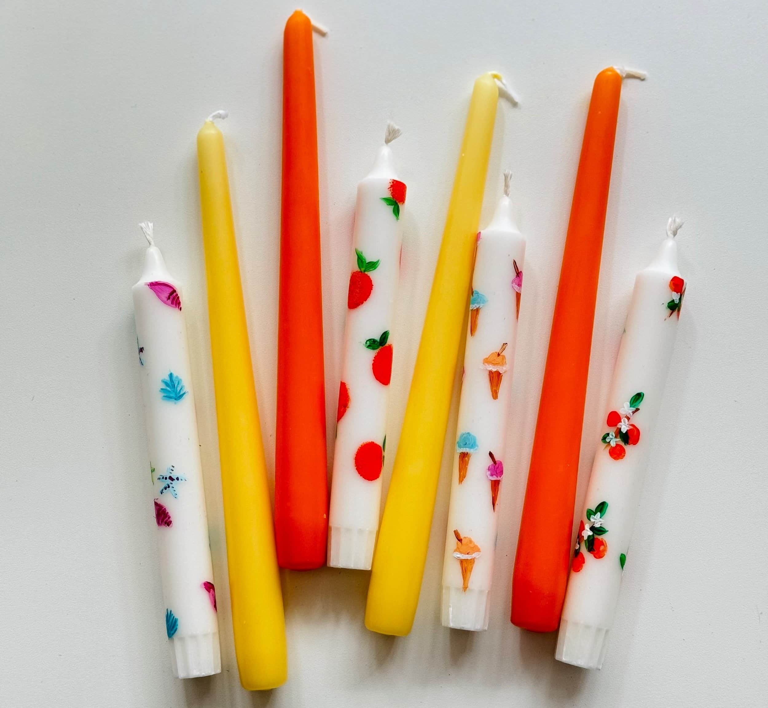 Bunte Kerzen in weiß, gelb und orange bemalt mit Symbolen wie orangen, Muscheln und Eis