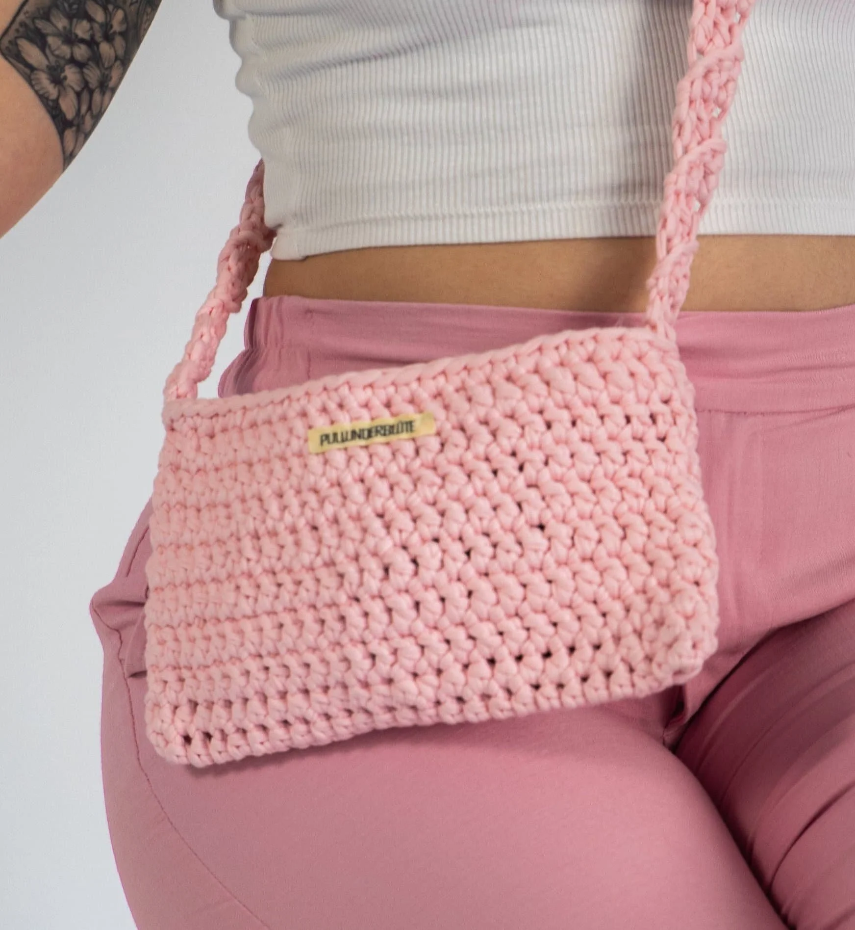 Selbstgehäckelte Umhangtasche in rosa auf dem Körper einer Person in rosa Hose und weißem Top