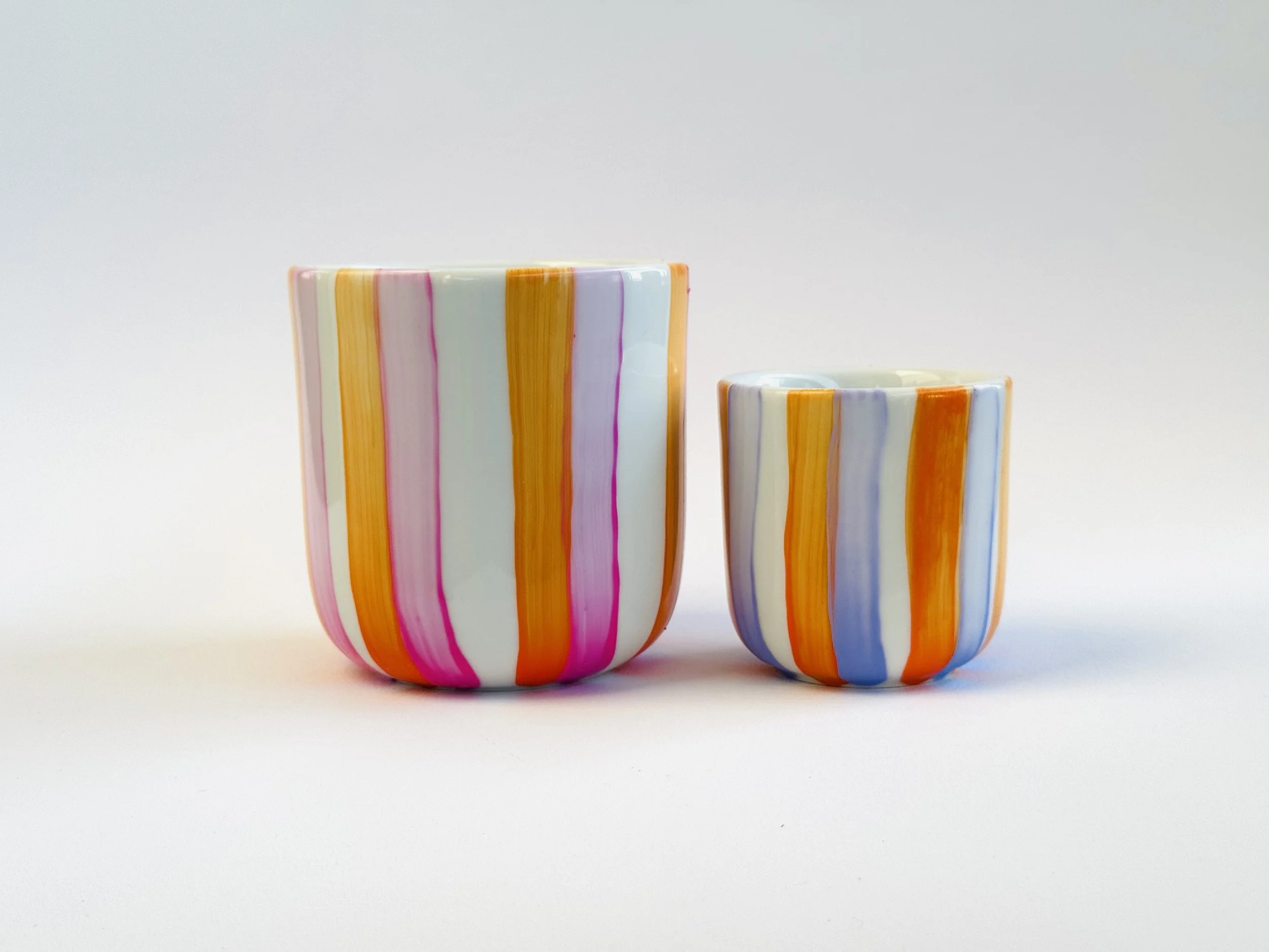 Zwei bunte Keramikvasen mit vertikalen Streifen in Gelb, Orange, Pink, Blau und Weiß auf weißem Hintergrund.