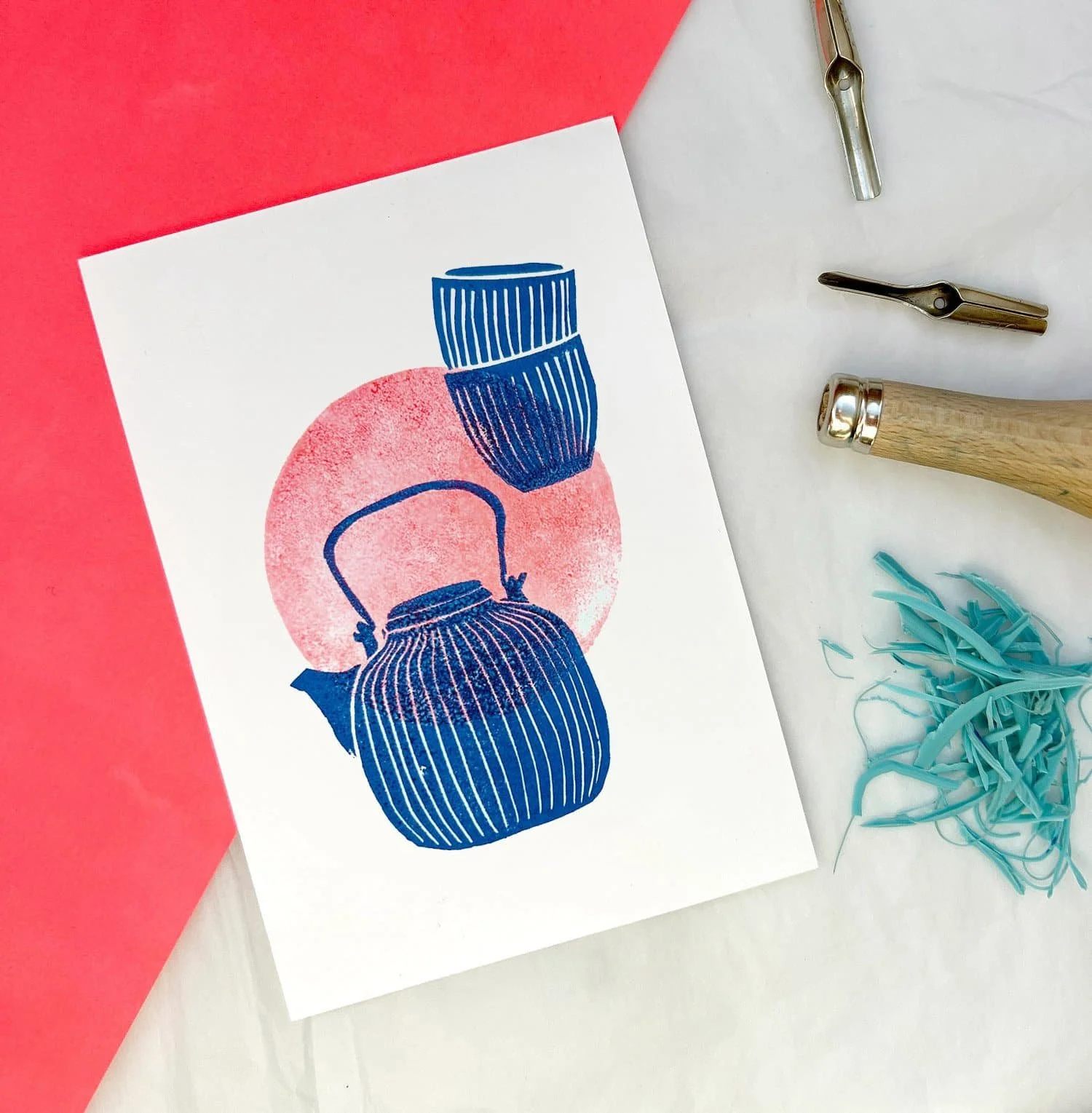 Illustration einer blauen Teekanne vor einem pinken Kreis auf weißem Hintergrund, umgeben von Druckwerkzeugen und Papier.