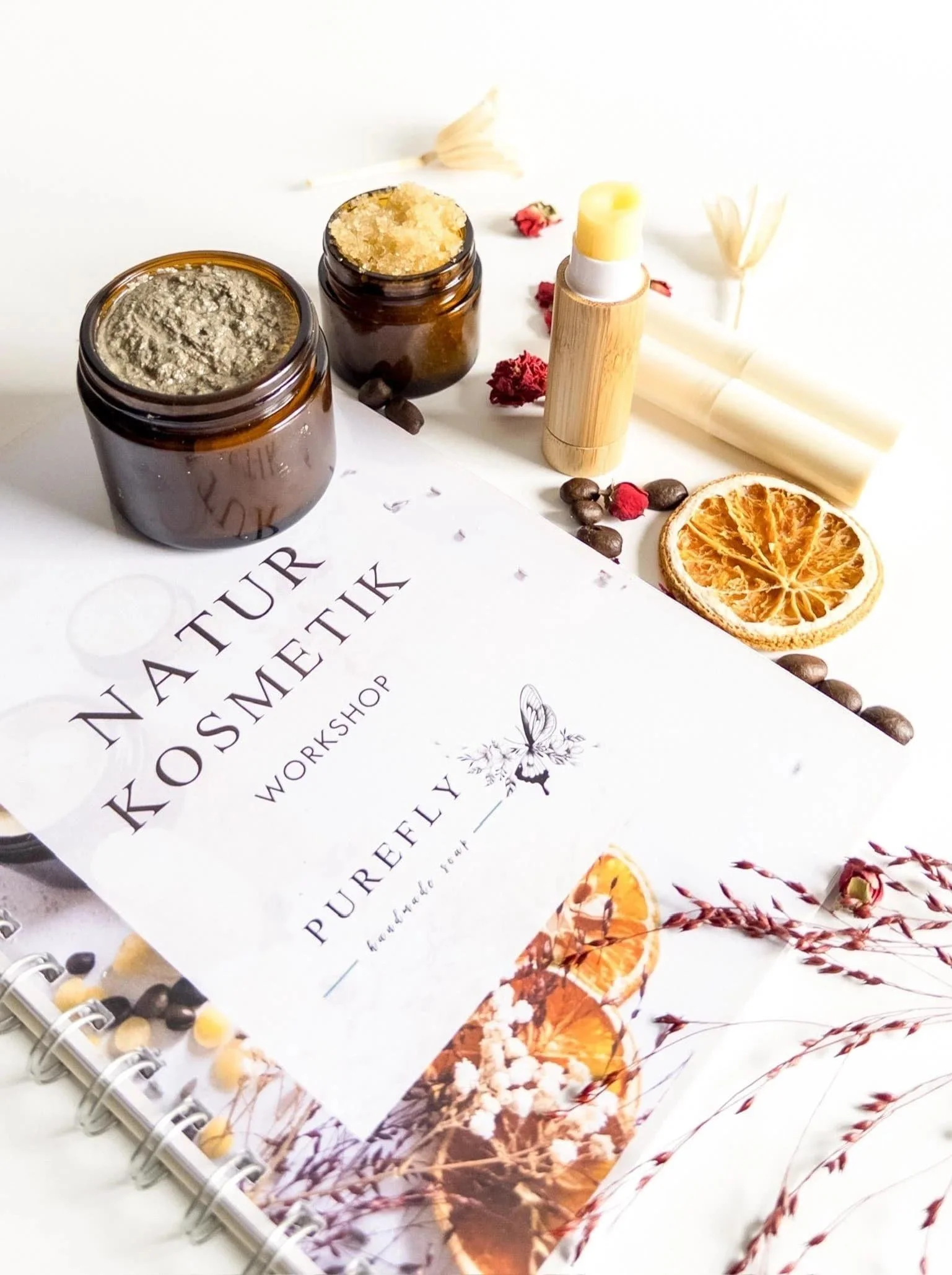 Heft über Naturkosmetik mit Dosen und Tuben mit Naturkosmetik sowie verschiedenen getrockneten Pflanzen