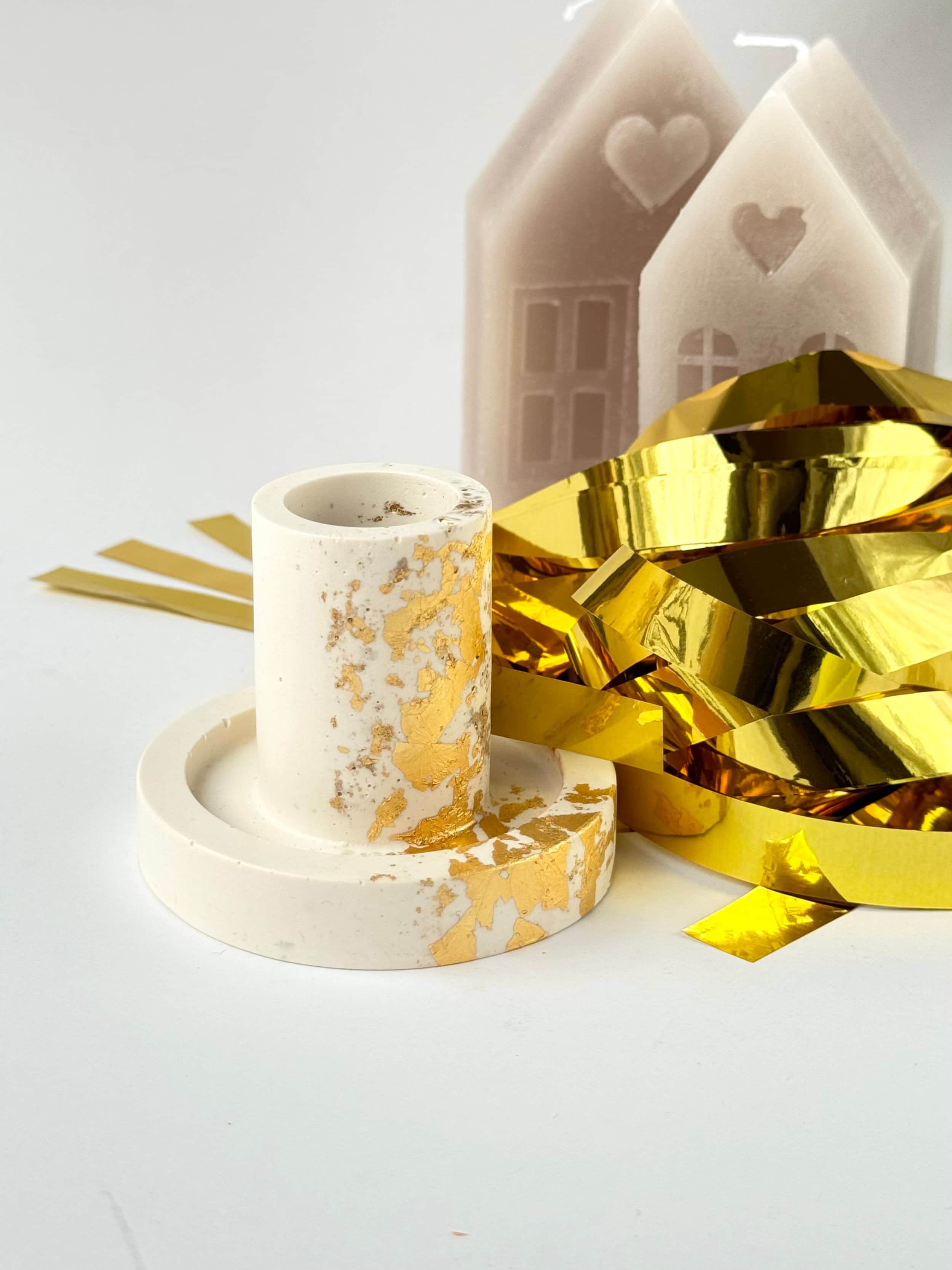 Jesmonite Kerzenständer in beige und gold mit goldener Banddeko und Wachshäusern im Hintergrund, auf weißem Untergrund