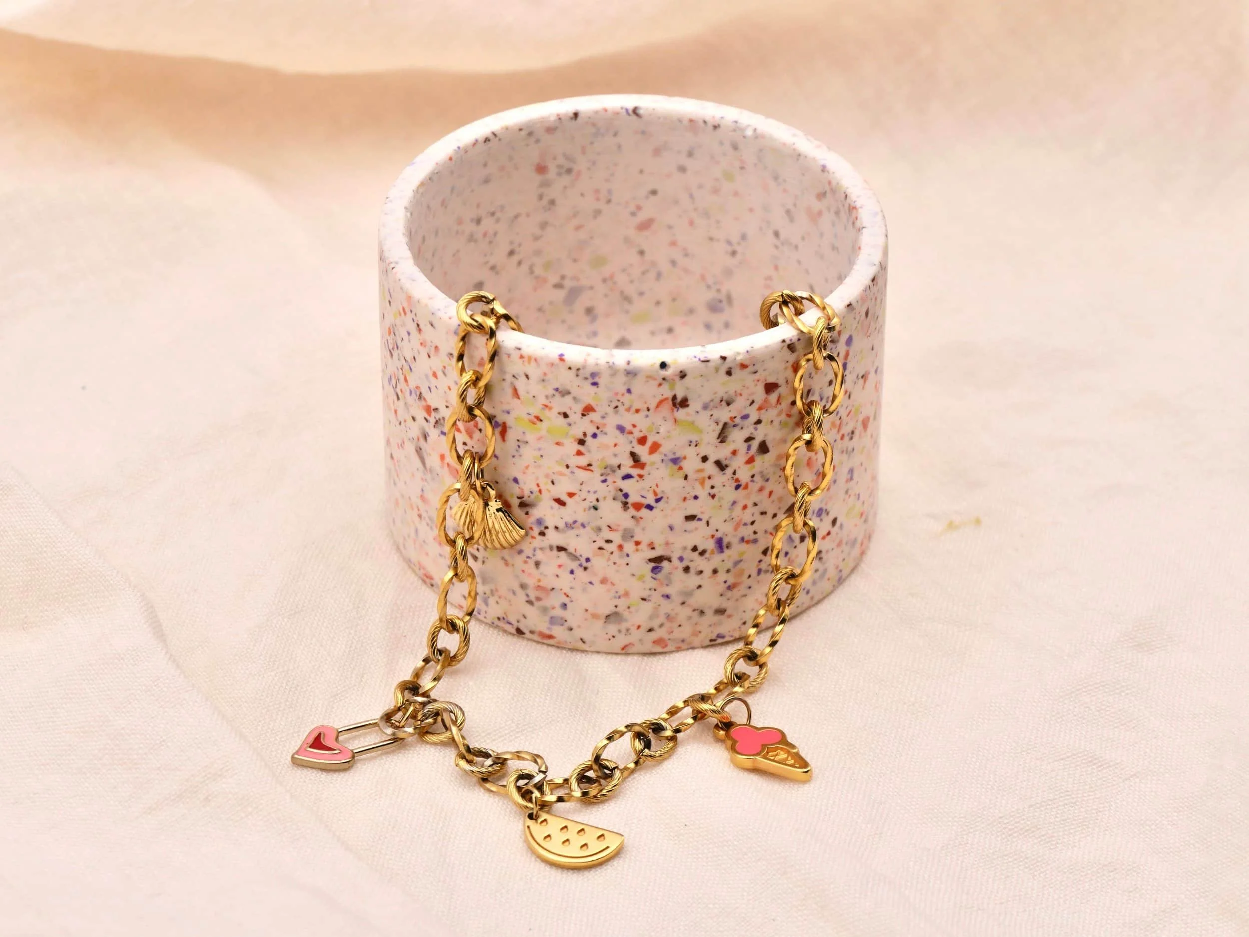 eine goldenen Gliederkette mit 3 Anhängern liegen in einem Terrazzo gemusterten Schälchen 