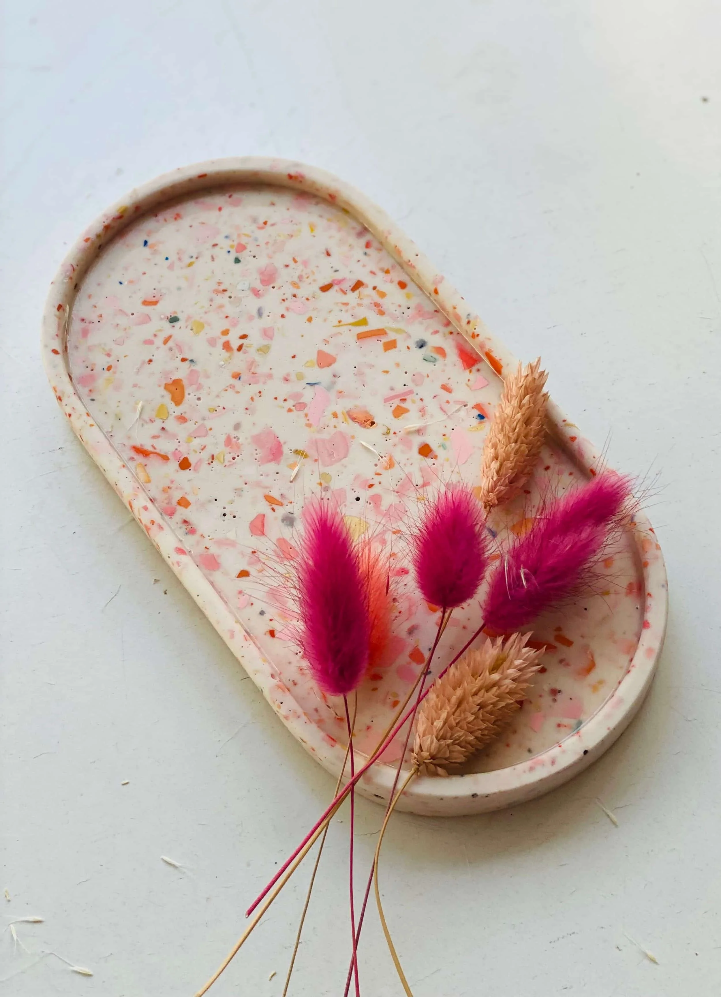 Ovale Schale in weiß mit buntem Terrazzo Muster in rosa, rot, oralem, blau und gelb. Trockenblumen in pink und beige