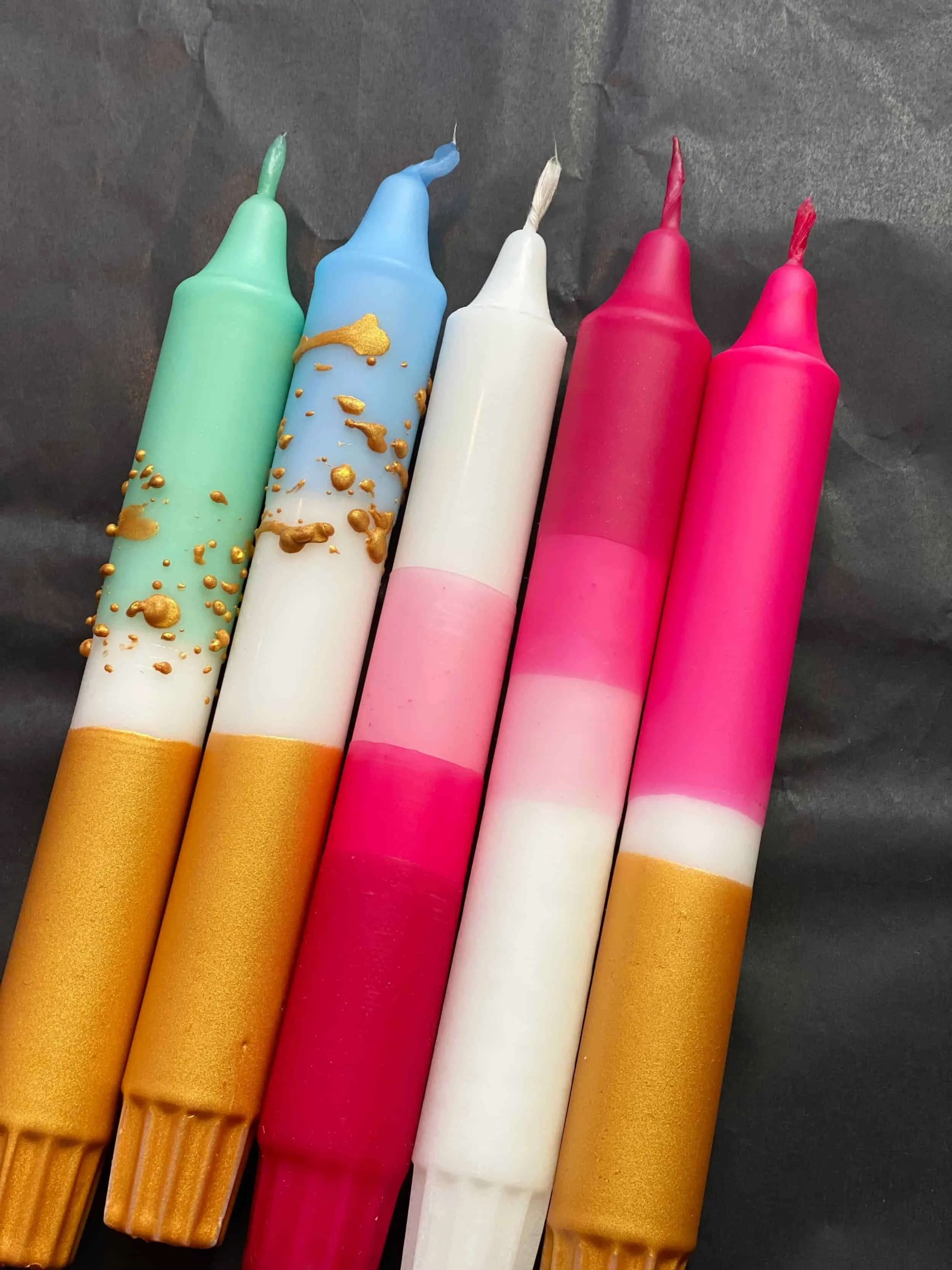 Fünf Dip Dye Kerzen in rosa, pink, gold, grün und blau mit goldenen Sprenkeln