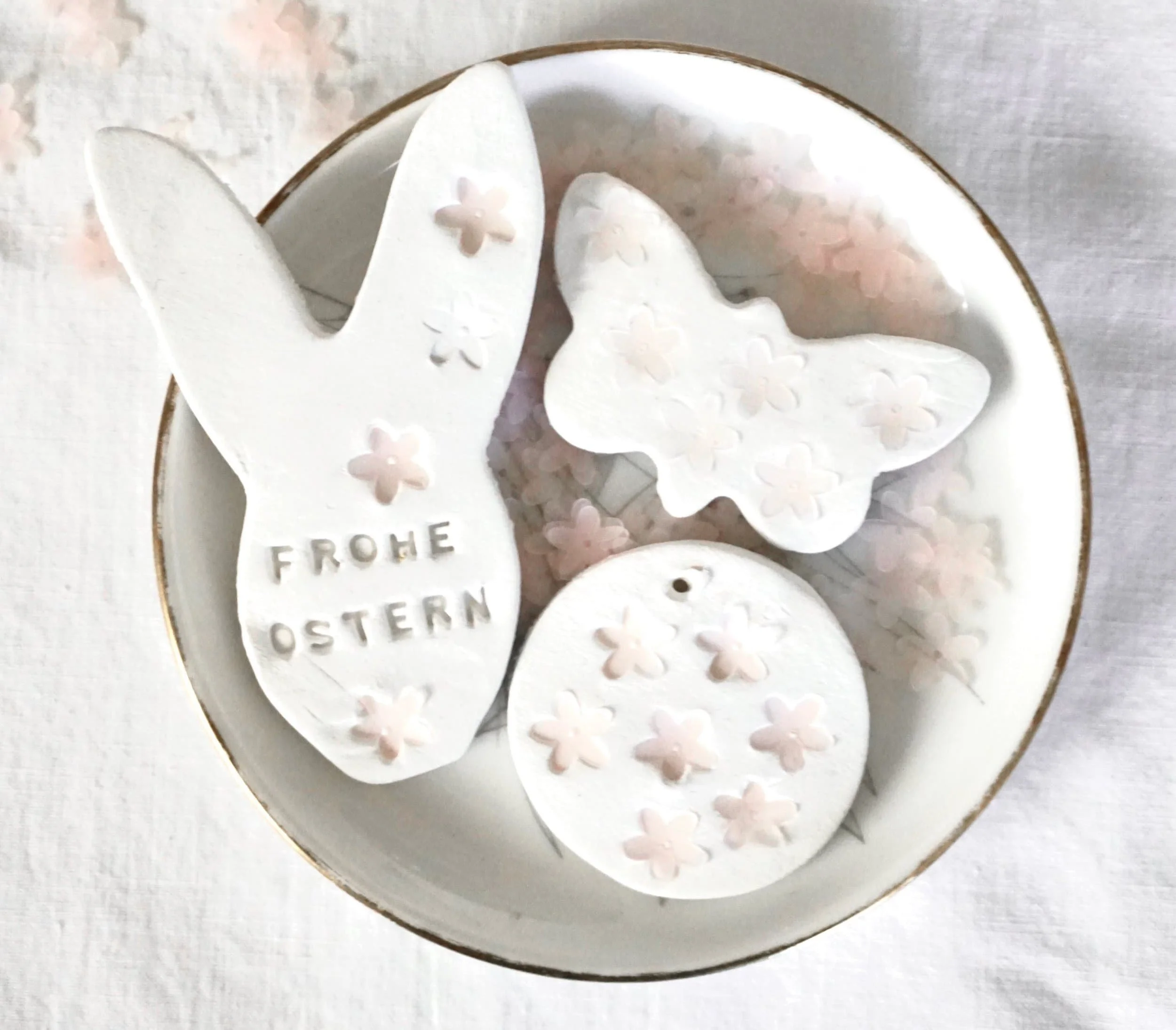 Osterdekoration aus weißer Fake Keramik in Form eines Hasen, eines Schmetterlings und eines Kreises, mit Blumenmustern und der Aufschrift "Frohe Ostern".