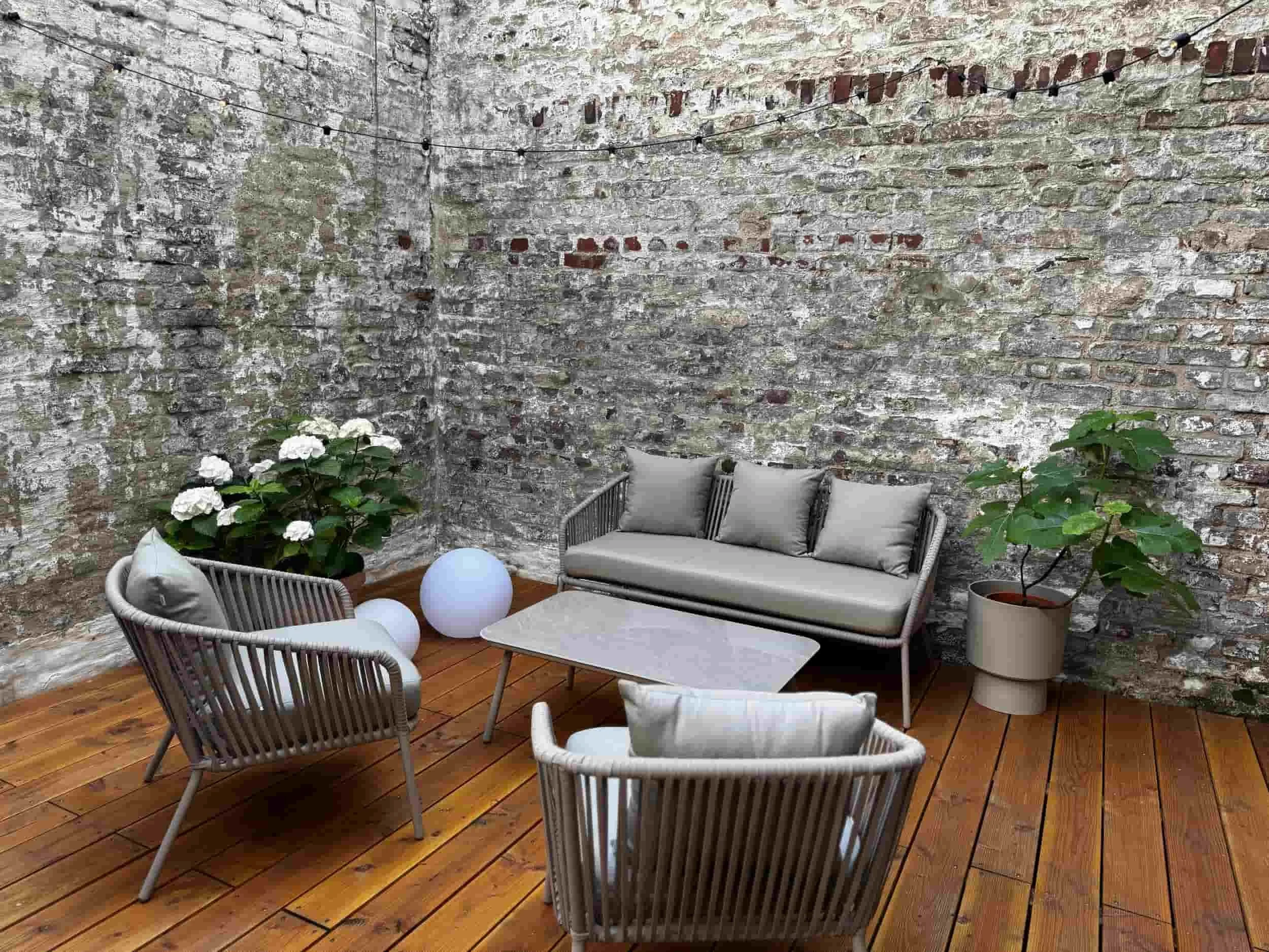 Terrasse mit einem Sofa, zwei Sessel und einem Beistelltisch, umgebend von zwei Pflanzen 