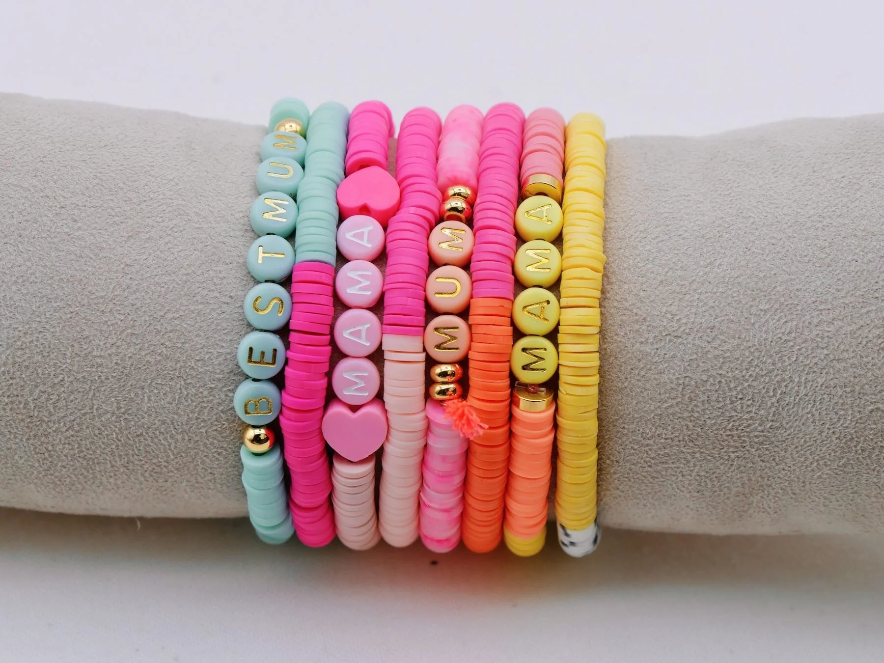 Sieben bunte Armbänder in rosa, rot, lila, weiß, türkis, gelb, pink mit Herzen, Quasten und Buchstaben. Perlenbuchstaben 'Best Mum', 'Mama', 'Mum', 'Mama'