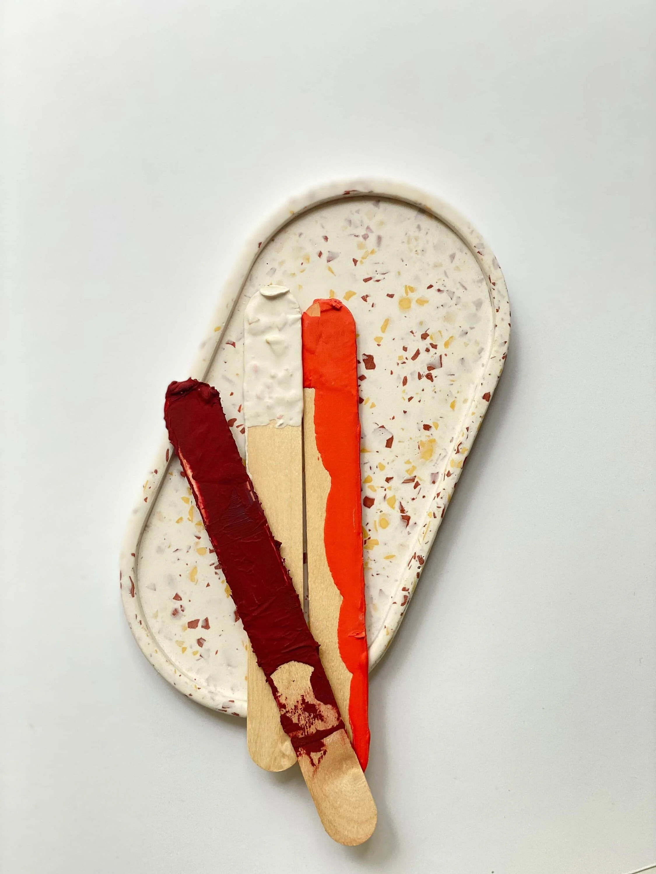 Ovale naturfarbene Schale mit Terrazzo Muster in beige, braun. Bunte Holzspatel umhüllt mir weiß, rot, dunkelrot