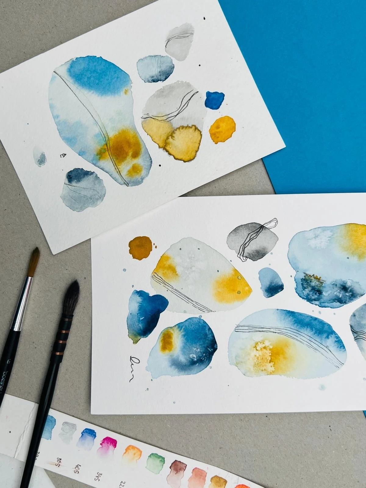 Abstraktes buntes Aquarellbild in blau und gelb, zwei Pinsel, Aquarellkasten