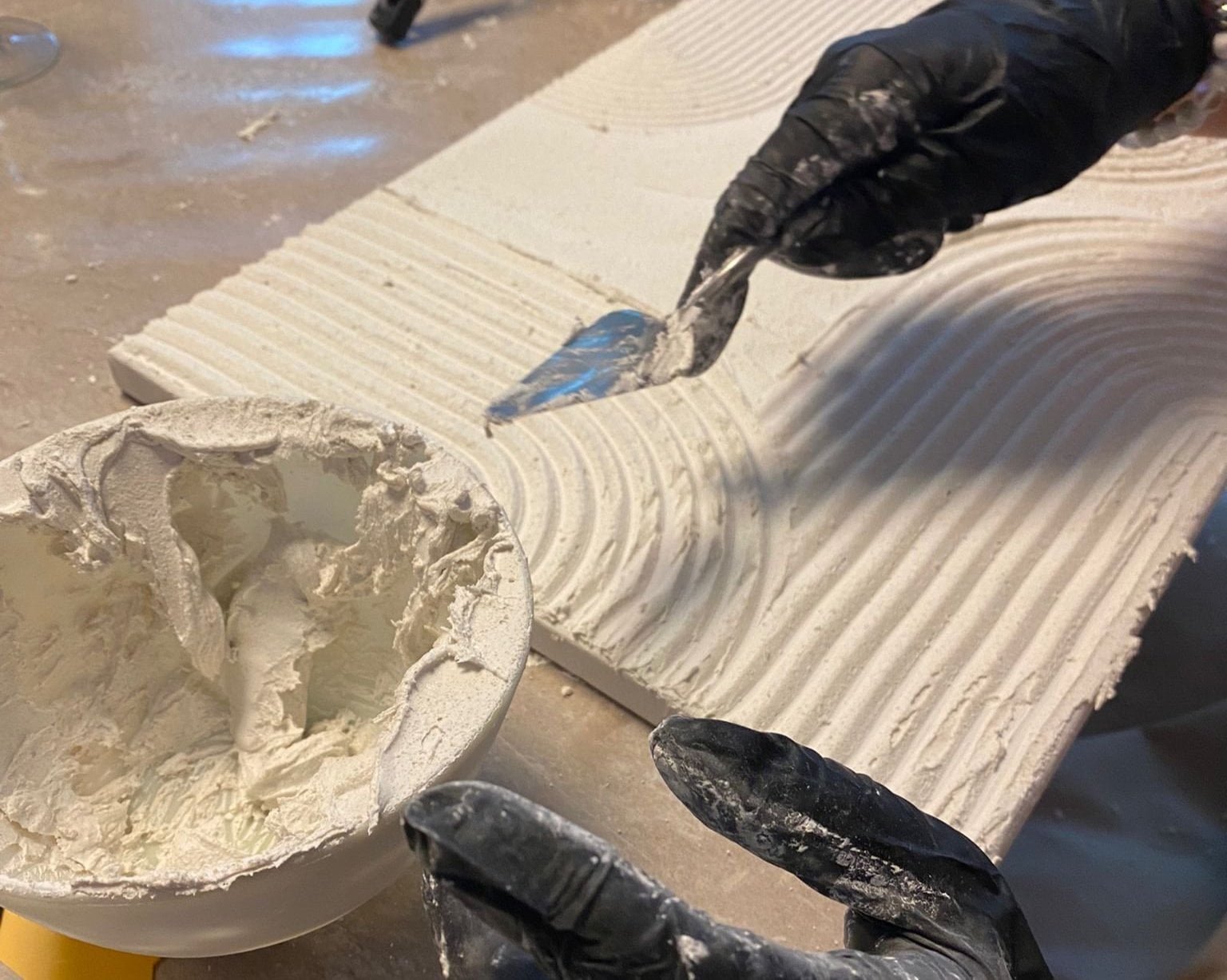 Strukturbild mit Kurven drauf, daneben eine Schale mit Strukturpaste sowie zwei Hände, die einen Spachtel halten