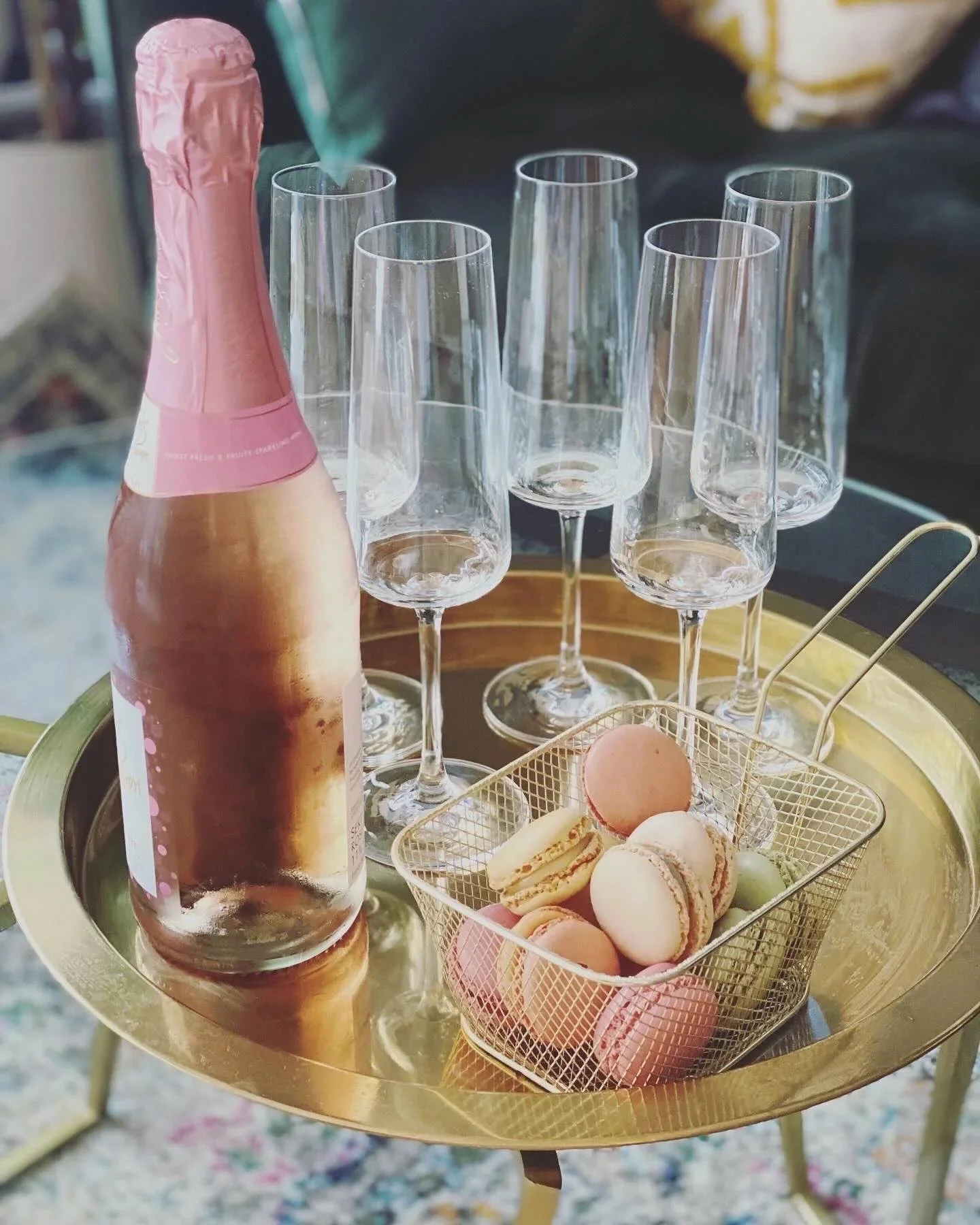 Flasche Rose-Sekt mit mehreren Sektgläsern daneben eine Schale mit bunten Macarons auf einem goldenen Tablett