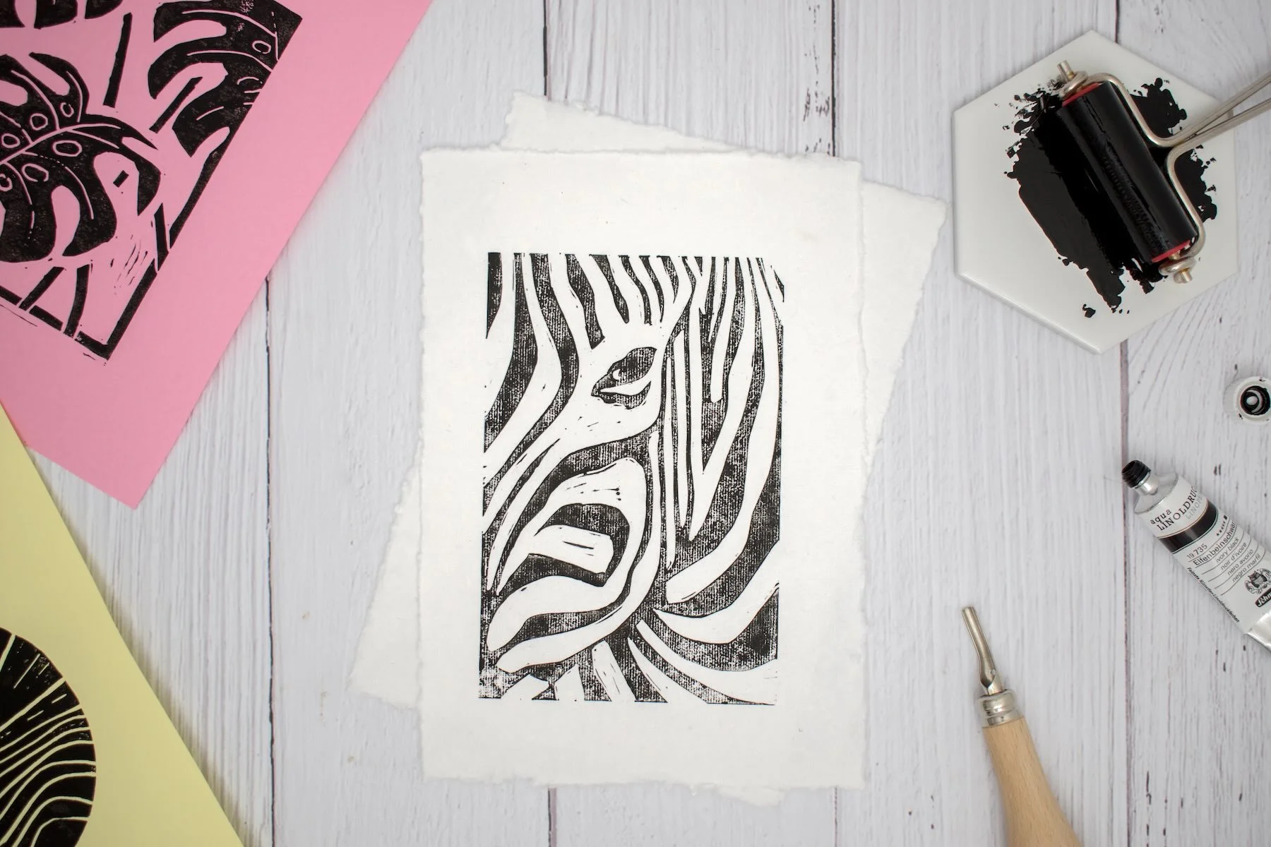 Schwarzer Druck eines Zebra Kopfes auf weißem Papier , drumherum liegen Werkzeuge, Tinte für Linoldruck