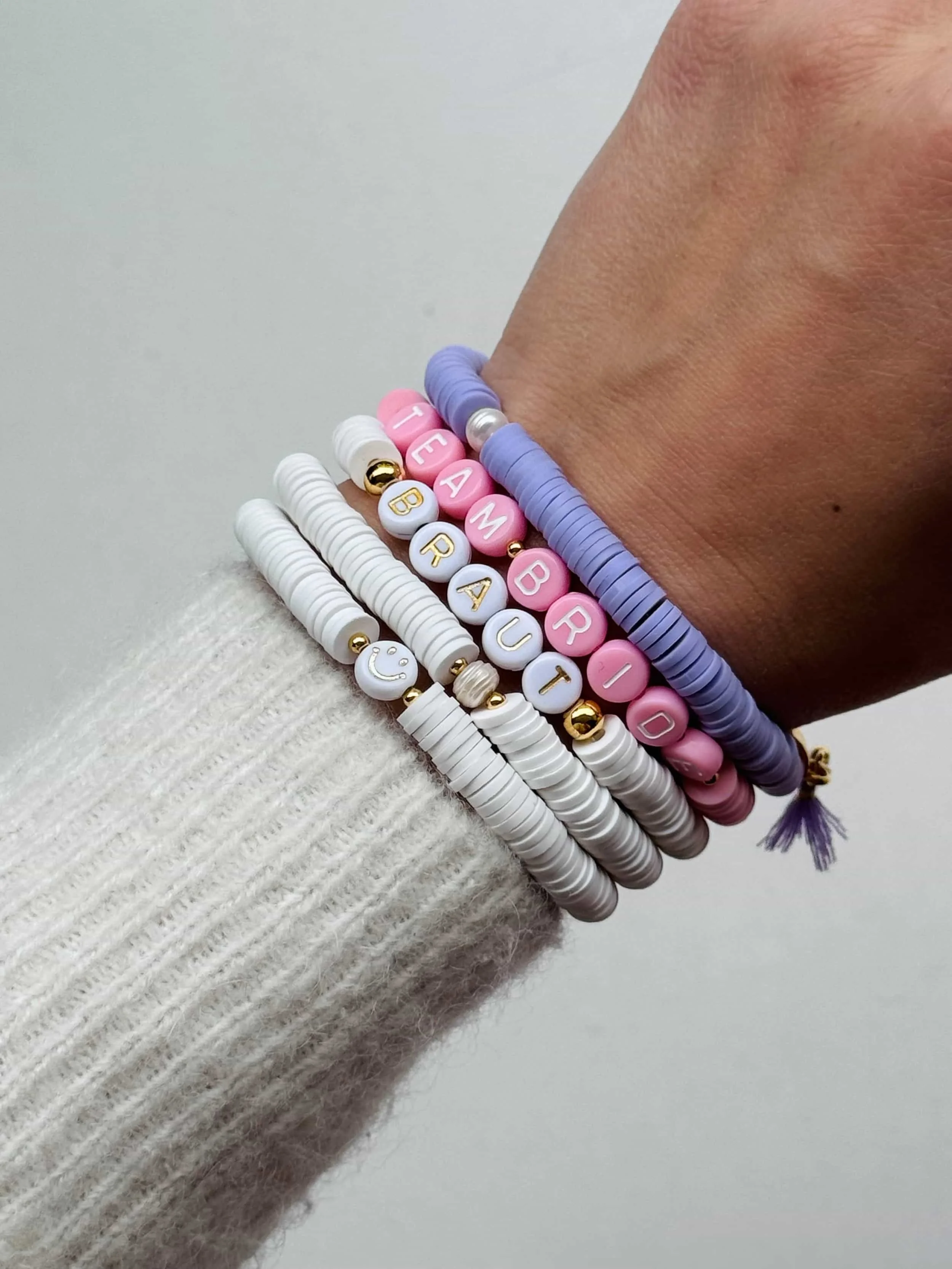 Mehrere Armbänder mit Katsukiperlen und Buchstaben, die den Namen 'TEAM BRIDE' bilden, an einem Handgelenk.