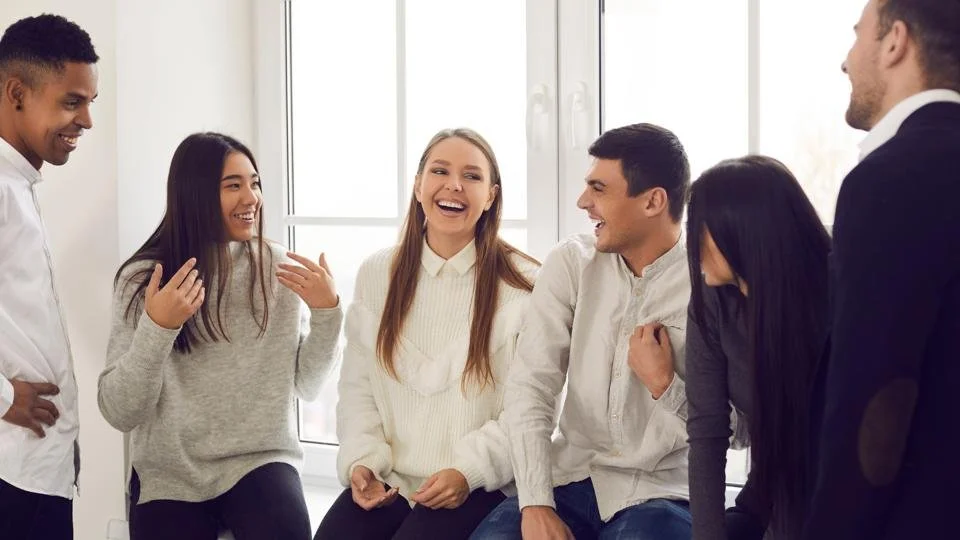 Grupo de personas riendo y conversando en una sala bien iluminada.