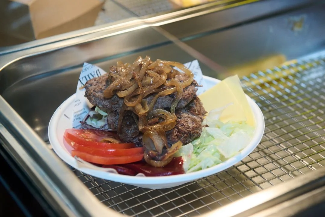 Fried meat with sautéed onions on top, served with sliced tomato, lettuce, and a slice of yellow cheese in a white bowl.