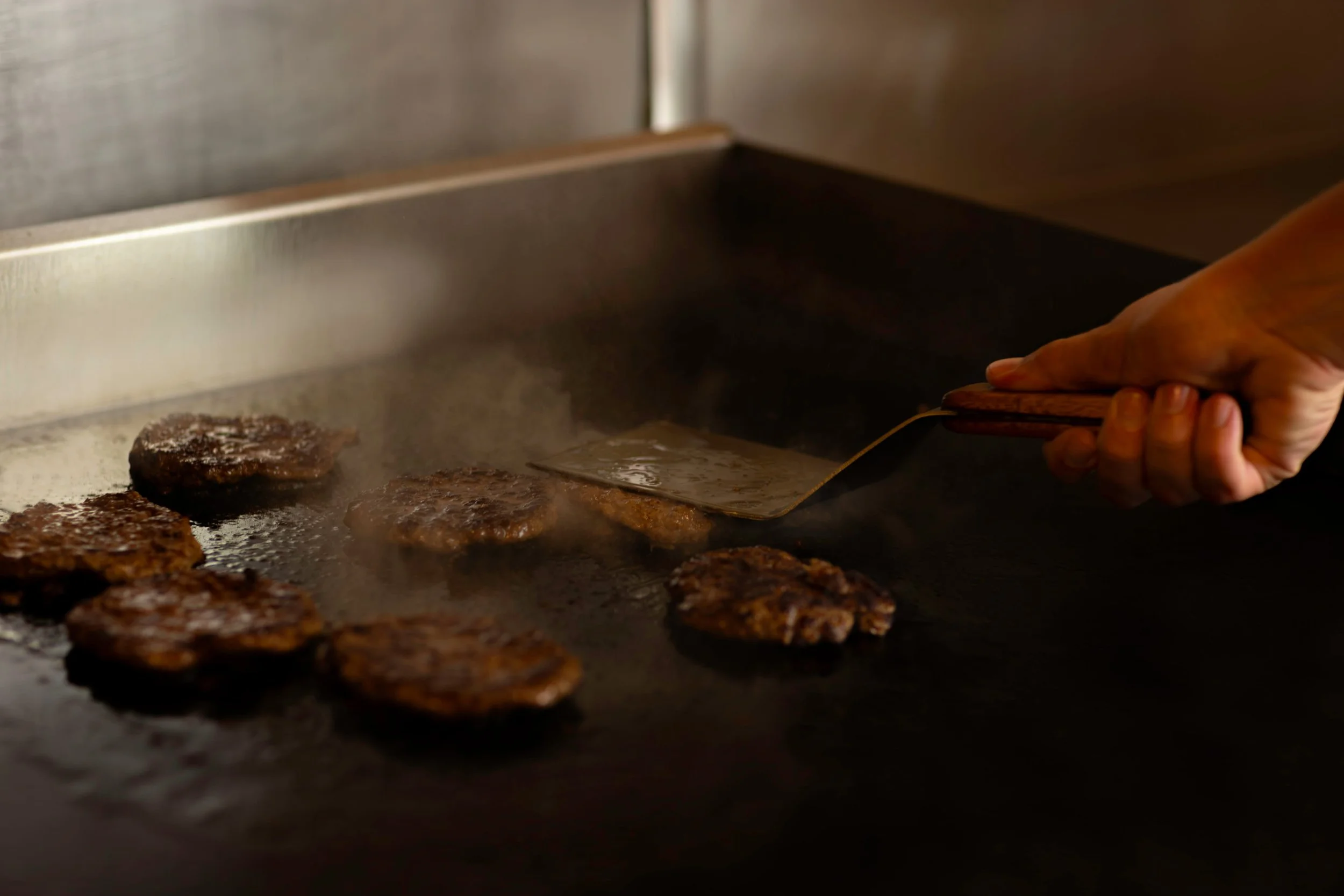 A person flipping burger patties on a flat grill.