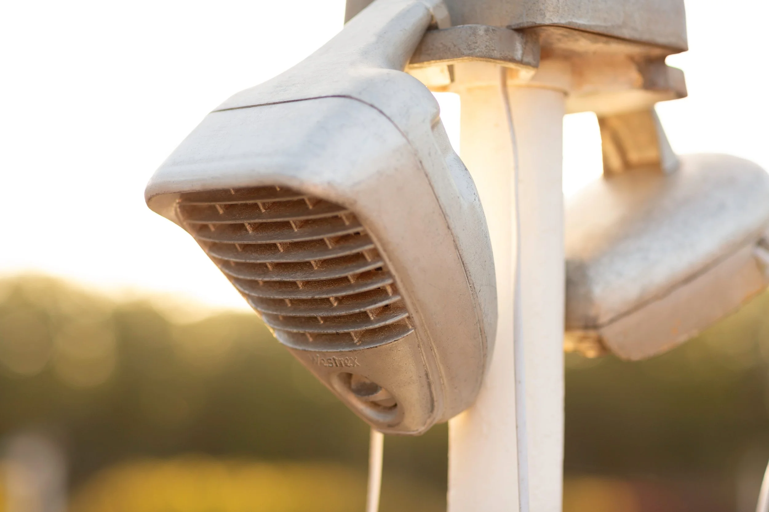 Close-up of a white plastic weatherproof electrical connector mounted on a white surface with sunlight shining through the opening.