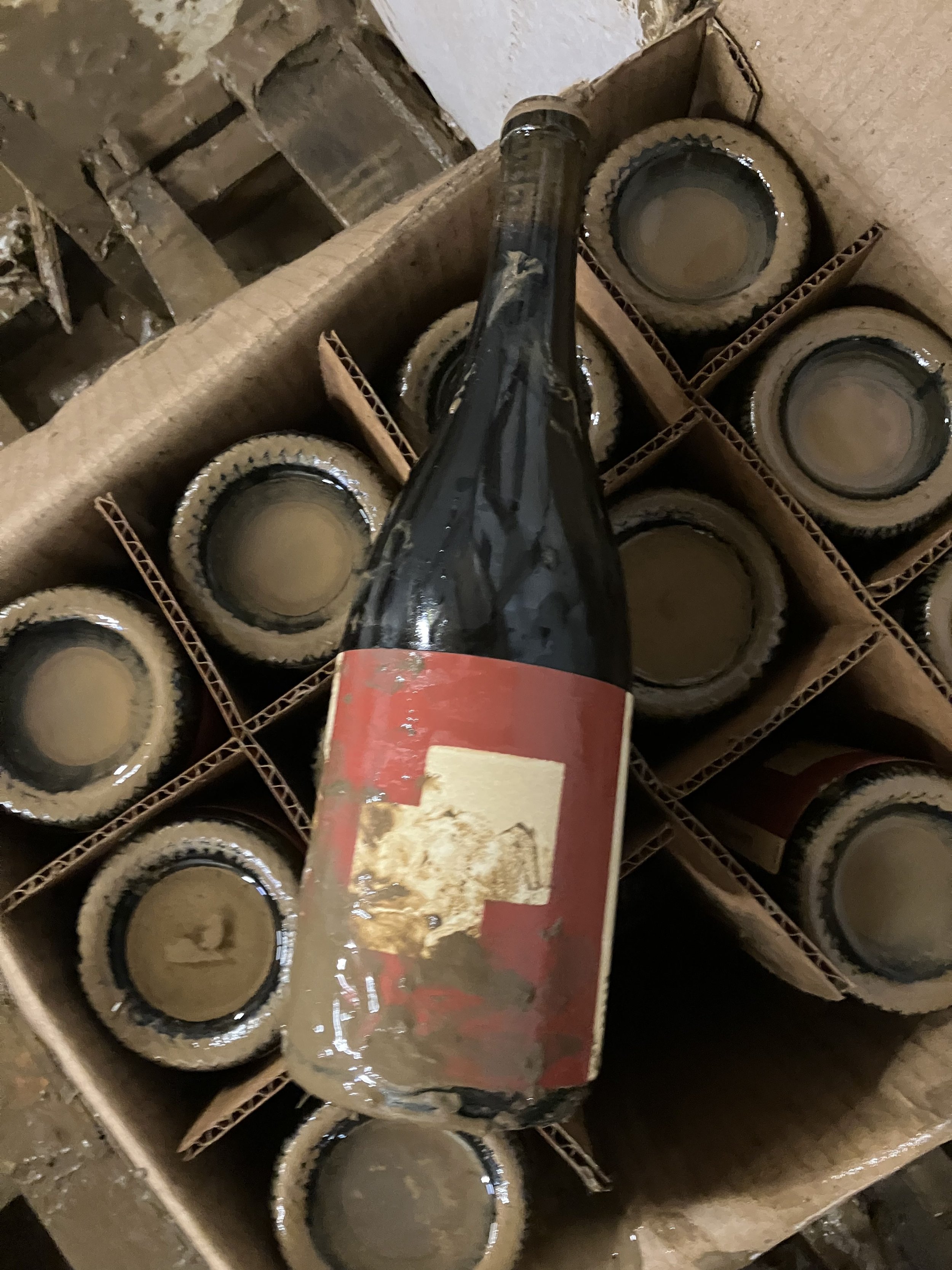 Bottle of wine covered in mud sitting on a case of wine