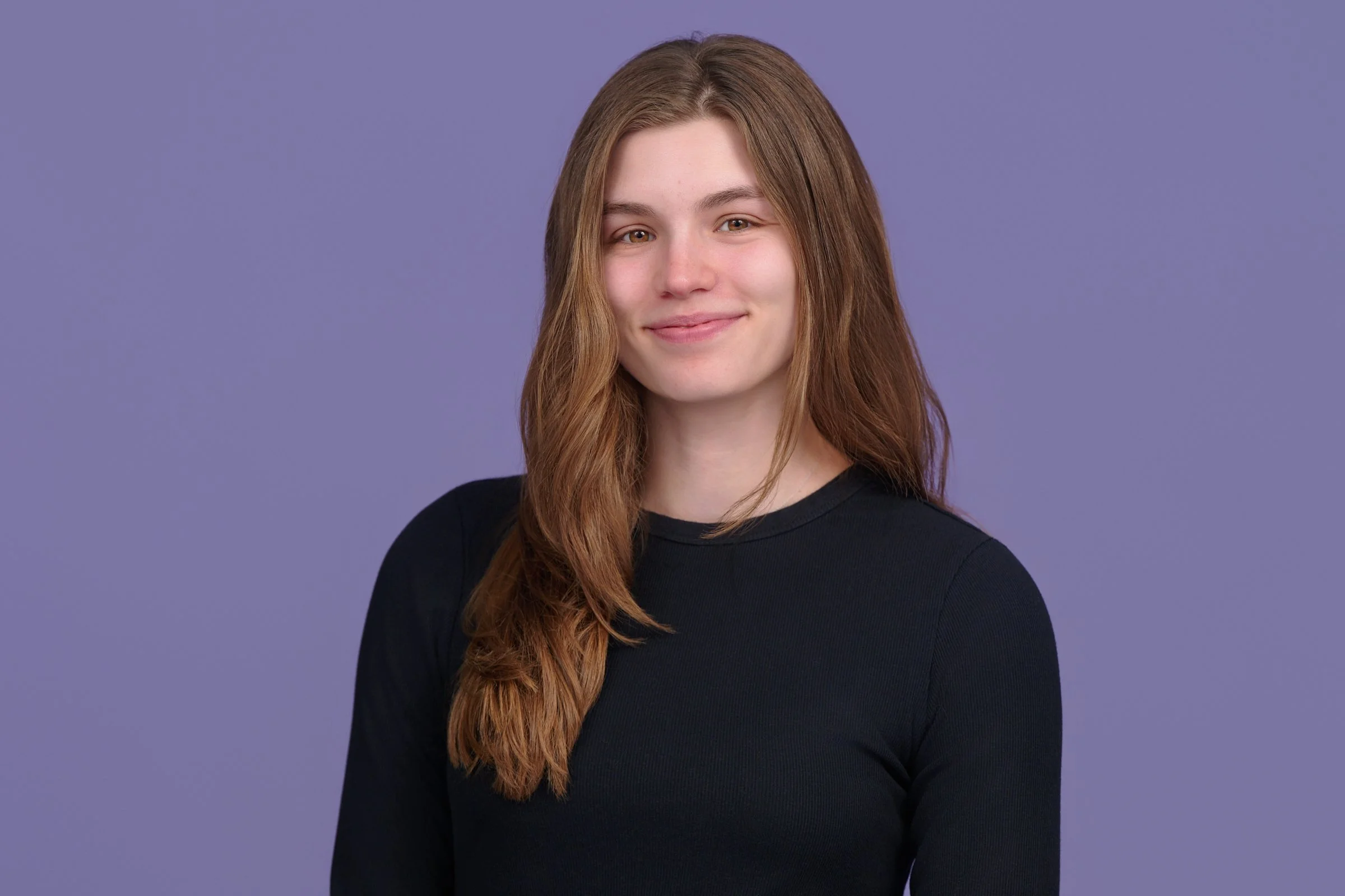 A young woman smiling on the steps outside her house, wearing a graduation sash with 'Rutgers' written on it, with autumn foliage in the background.