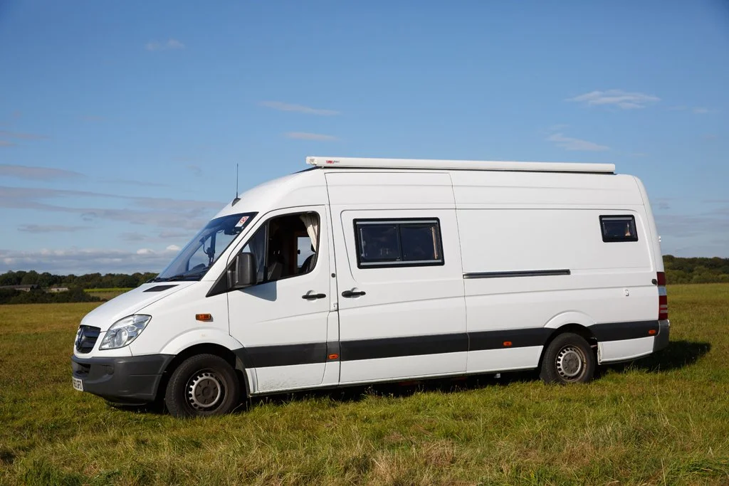 Azure parked in open countryside, showing the full side profile of this handcrafted campervan. Featuring a large side window, off-grid setup and classic Mercedes Sprinter body, Azure is ideal for relaxed campervan or motorhome hire from Bristol, perf