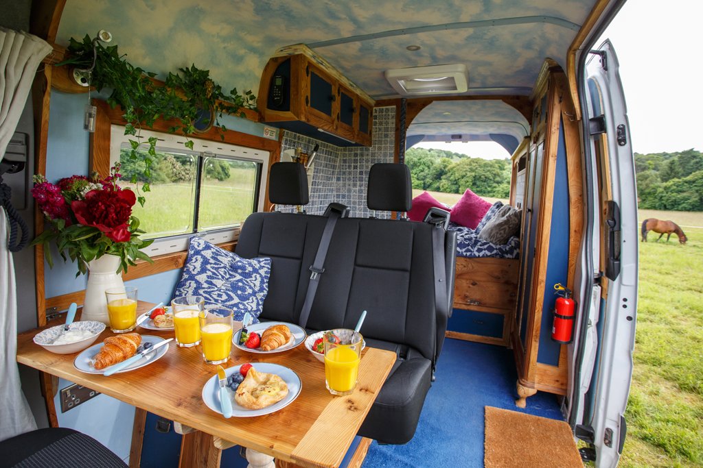 Bright and spacious dining area inside Azure, featuring a handmade wooden table, comfortable seating and countryside views through the open side door. Designed for relaxed meals and slow mornings, this welcoming interior makes Azure ideal for family 