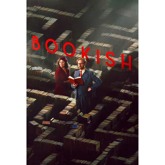 A man with a book and woman stand in rows of books arranged as a maze.