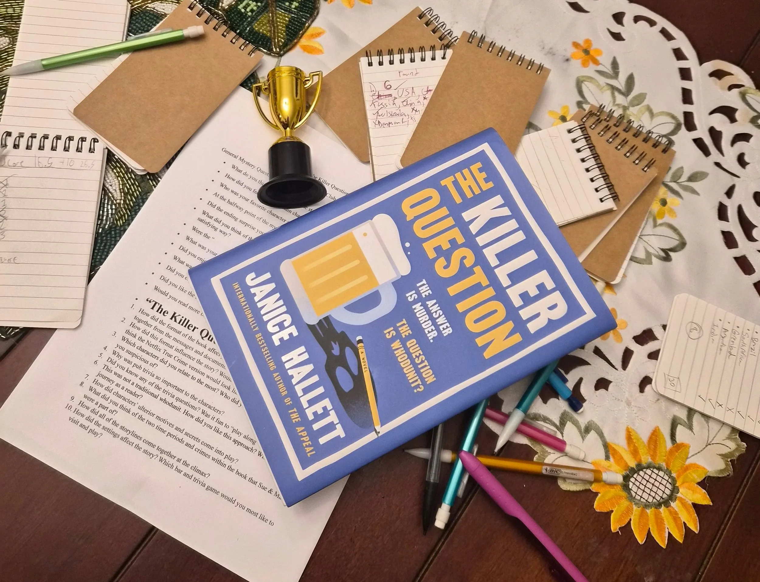 The book "The Killer Question" with notebooks, a trophy, and supplies for a trivia game.