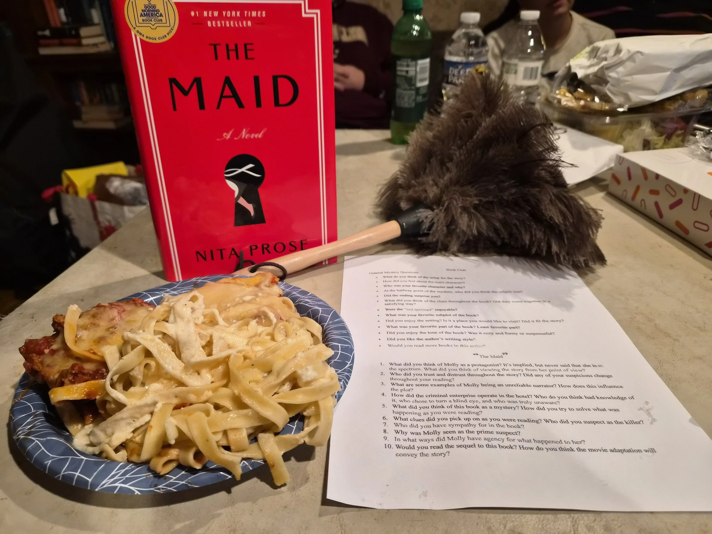 The book "The Maid" next to a feather duster and fettucine.